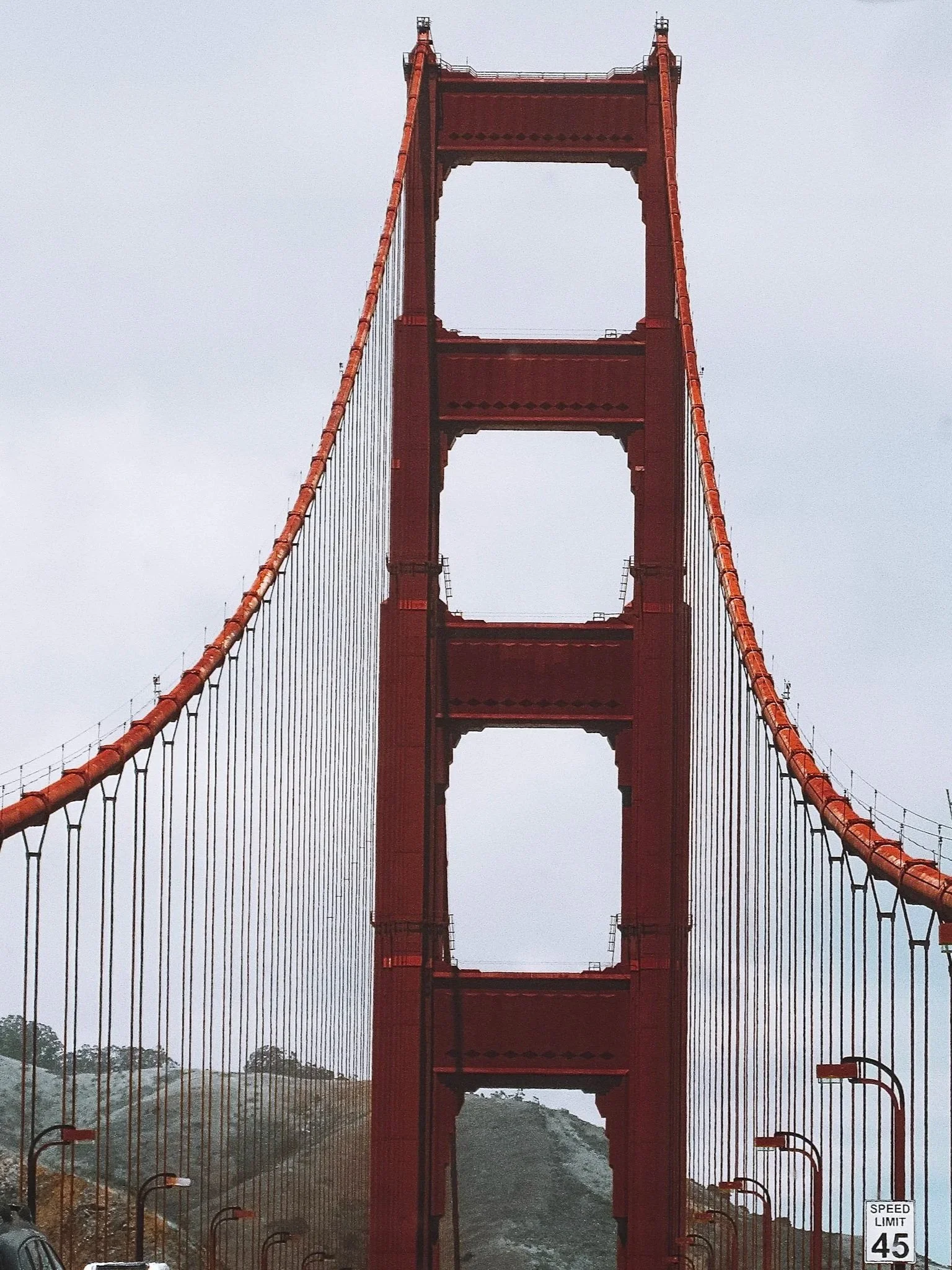 A view of the Golden Gate Bridge from below, showing the red tower and suspension cables against an overcast sky.