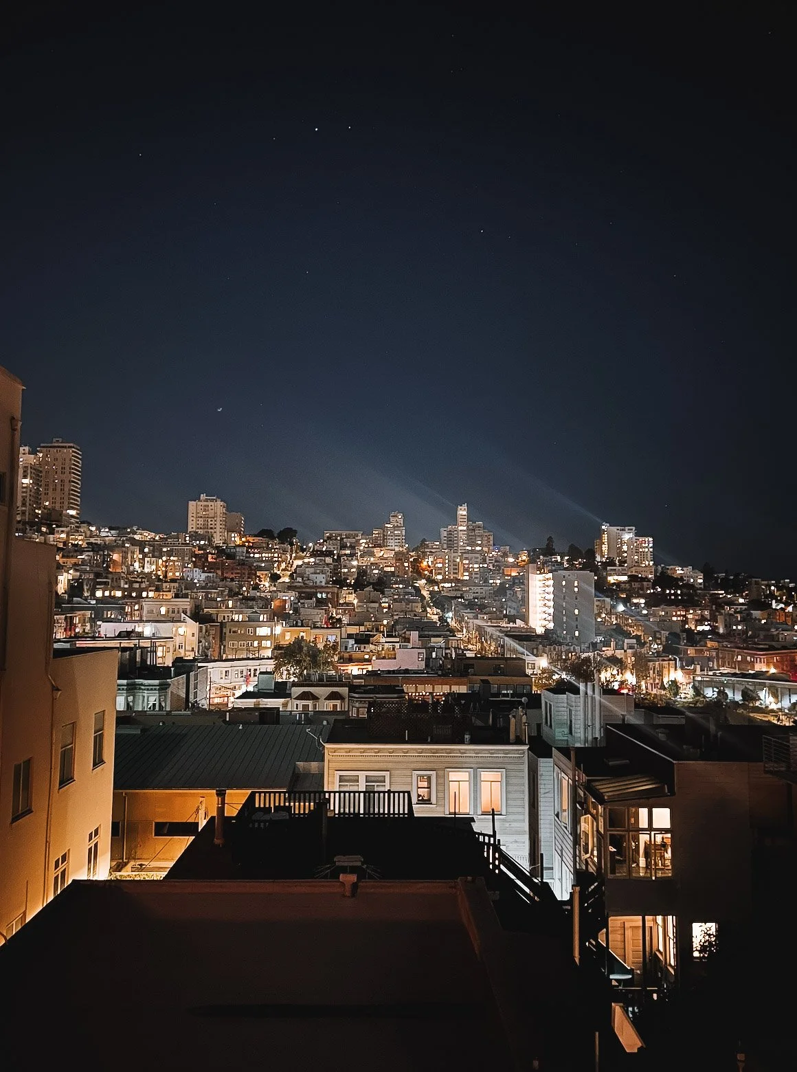 Nighttime cityscape view of San Francisco, with illuminated buildings and a clear, starry sky.