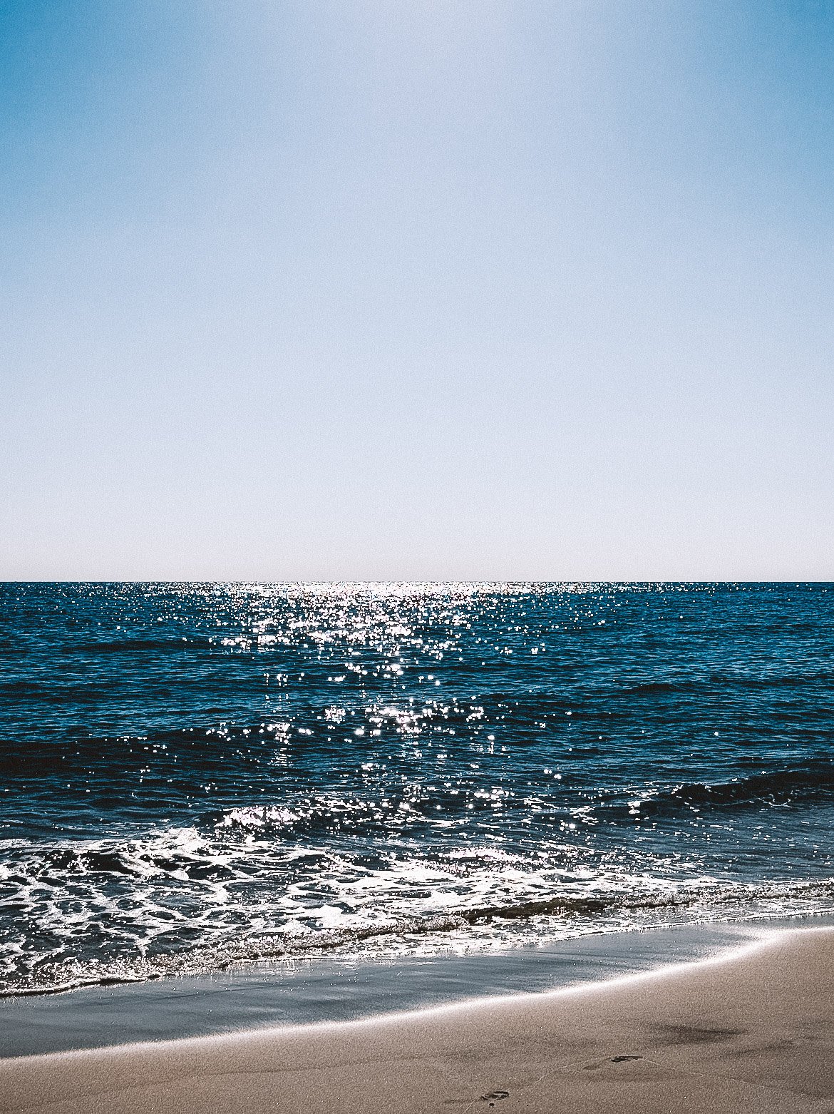 Sunny day at the beach with calm ocean waves and a clear blue sky.