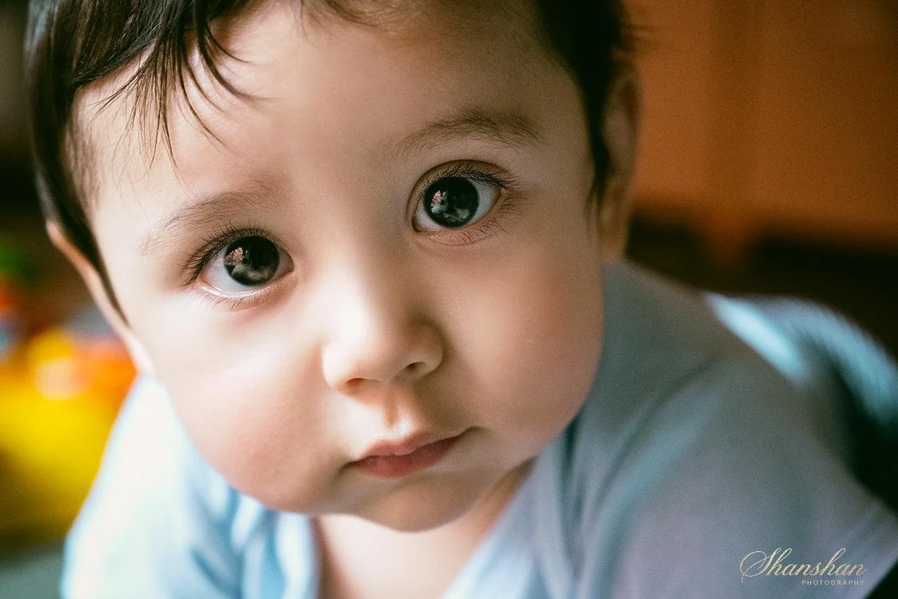 Close-up of a young child's face with large, expressive eyes, dark hair, and a curious expression.