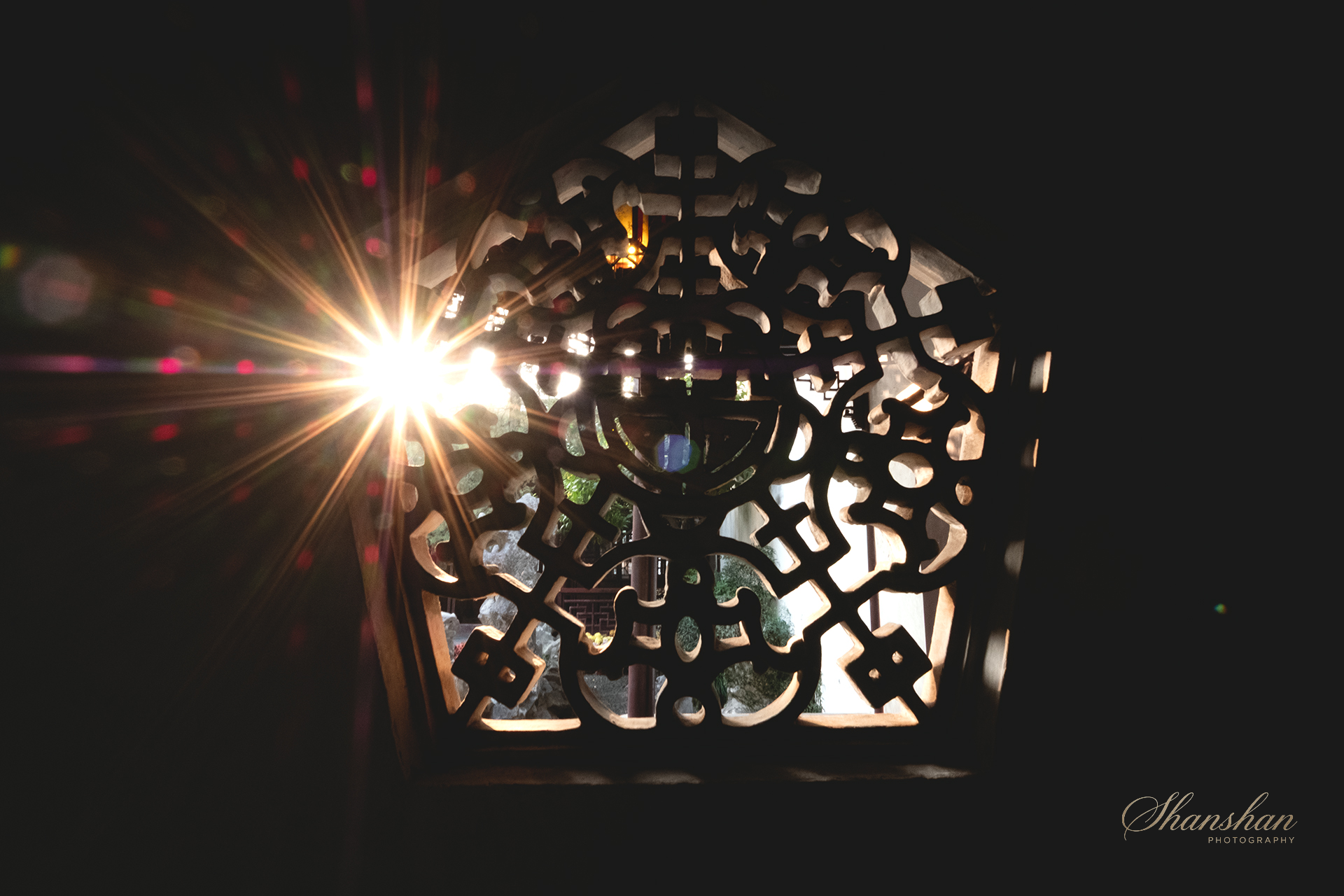 Sunlight shining through an intricately carved wooden panel, creating starburst and lens flare effects.