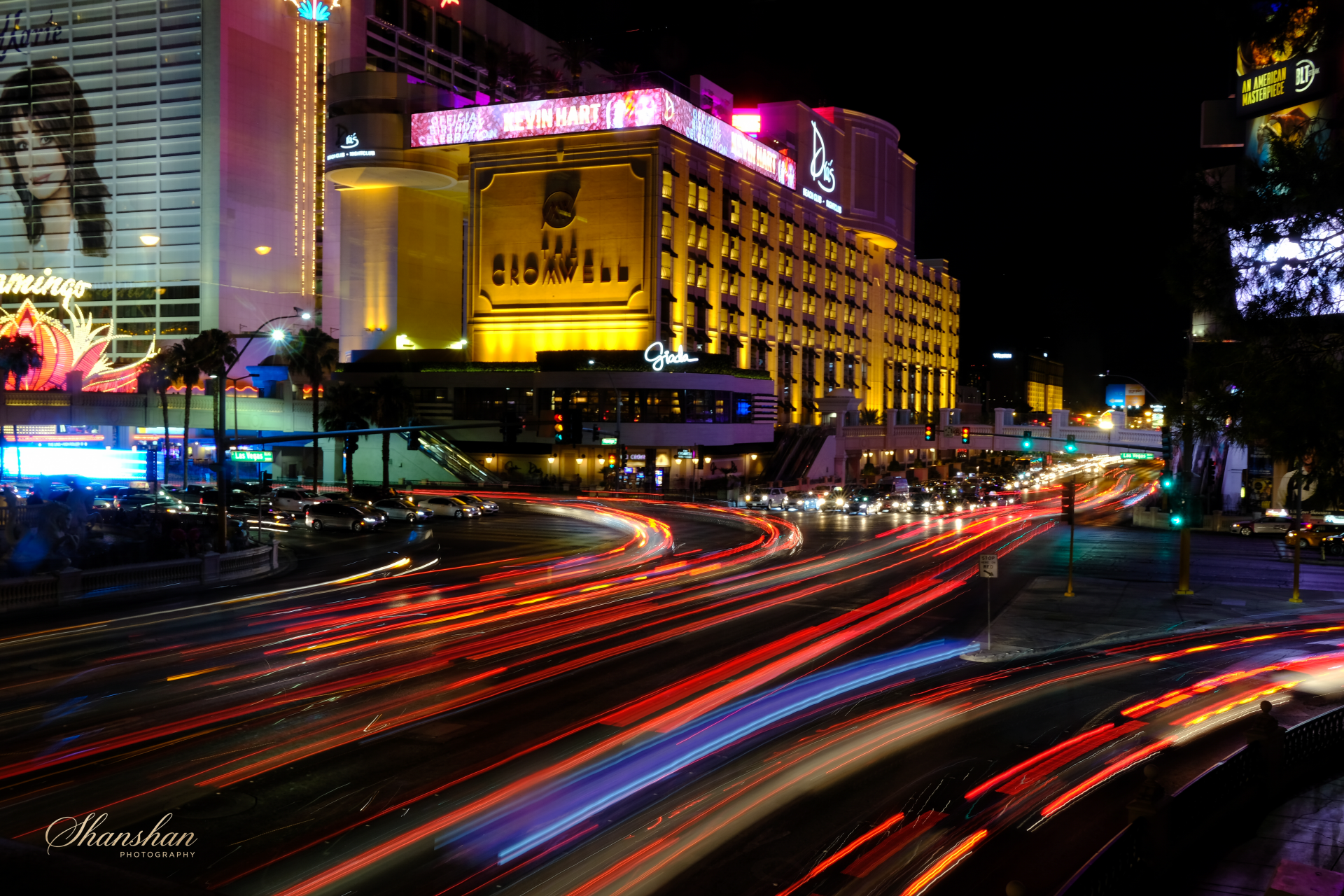 Nighttime scene of Las Vegas Strip with illuminated signage, buildings, and streaks of car lights on the road.