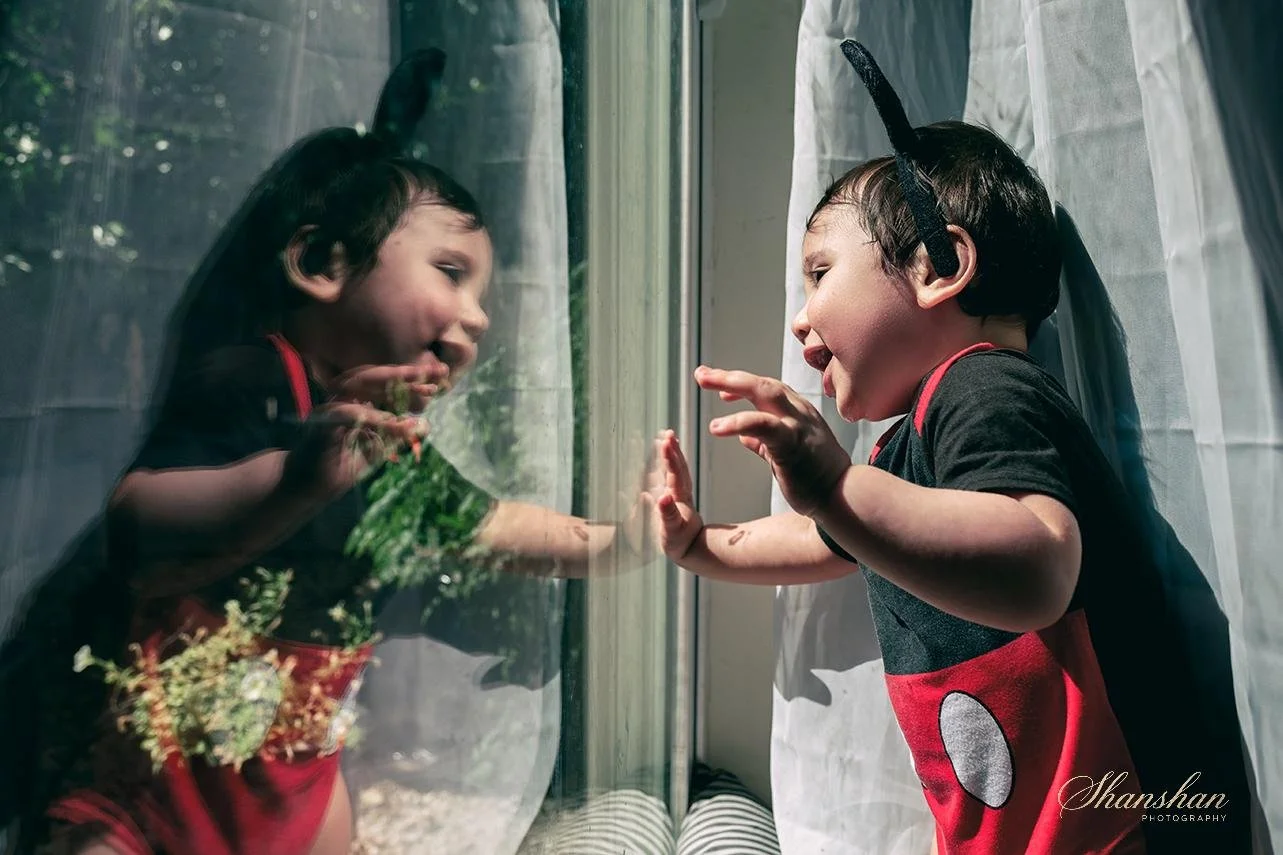 A young boy and girl are pressing their hands against a glass window, smiling and looking at each other, with reflections visible on the glass.