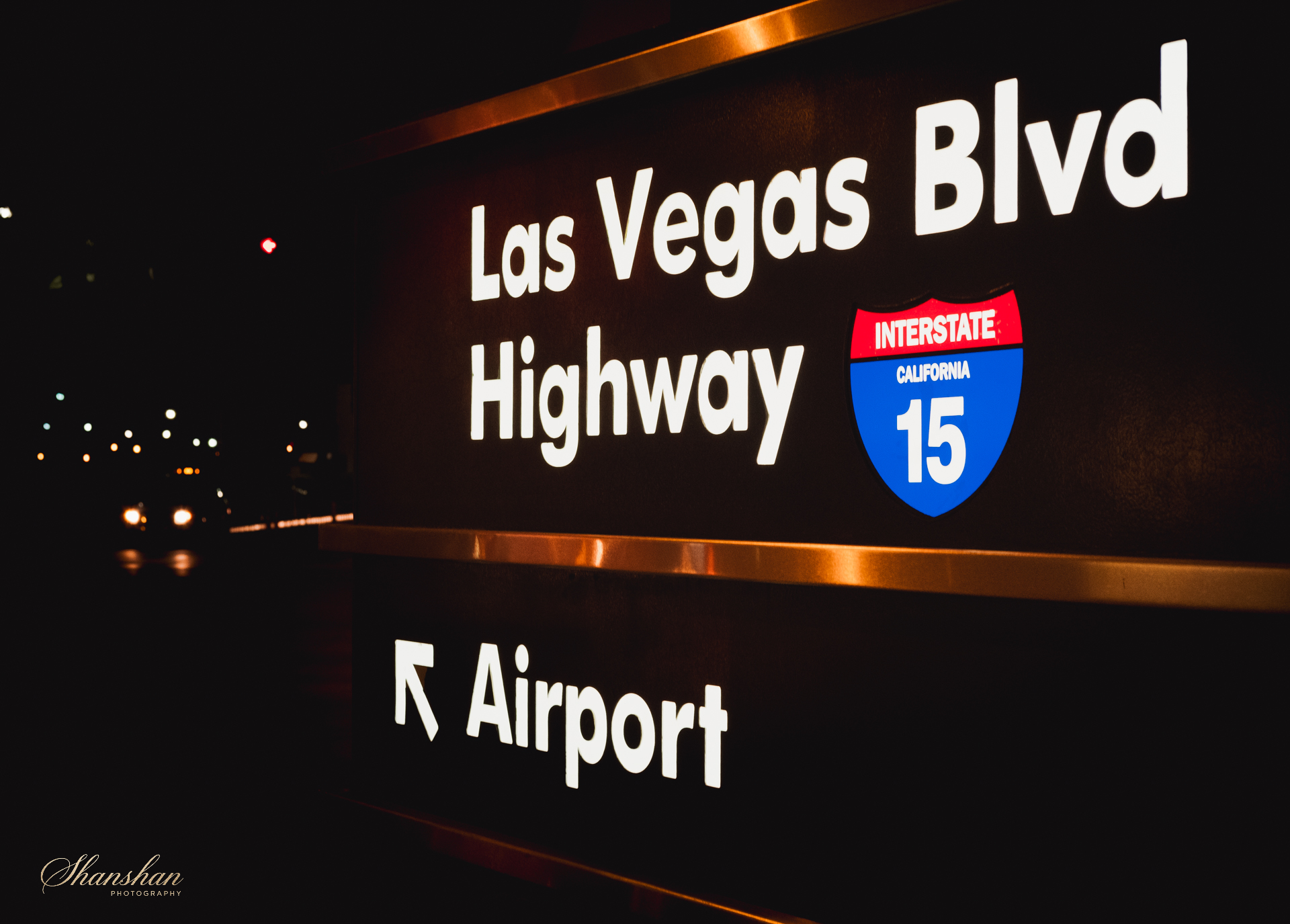 Nighttime illuminated sign for Las Vegas Boulevard Highway and Interstate 15, with a partial arrow and airport sign visible.