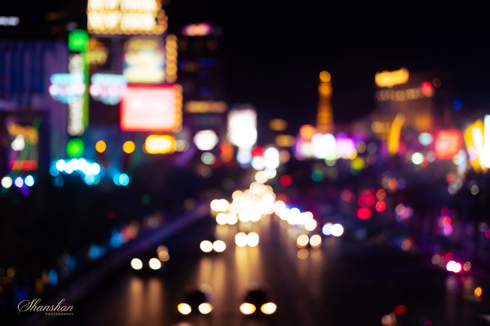 Blurry city lights at night with colorful neon signs and vehicle headlights and taillights on the road.