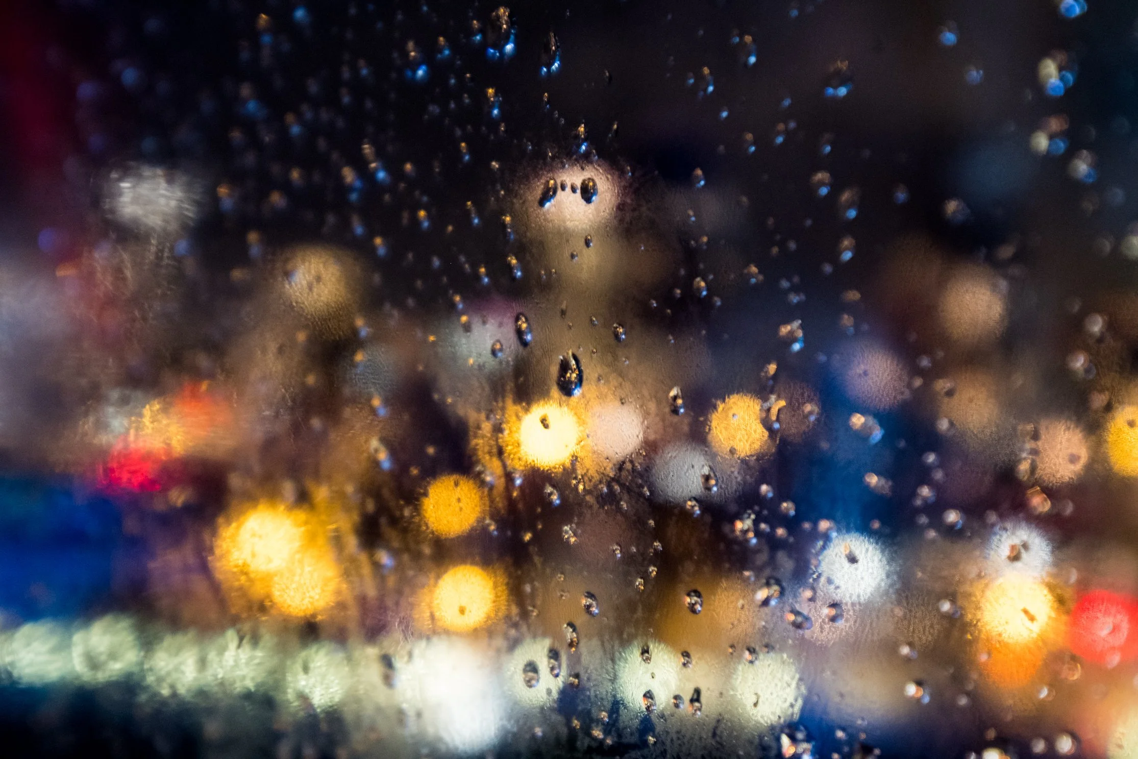 Rain droplets on a window with colorful, blurred city lights in the background at night.