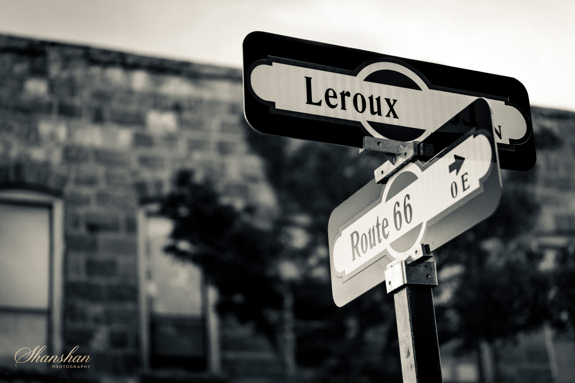Black and white street sign showing 'Leroux' at intersection with Route 66 in an urban area.
