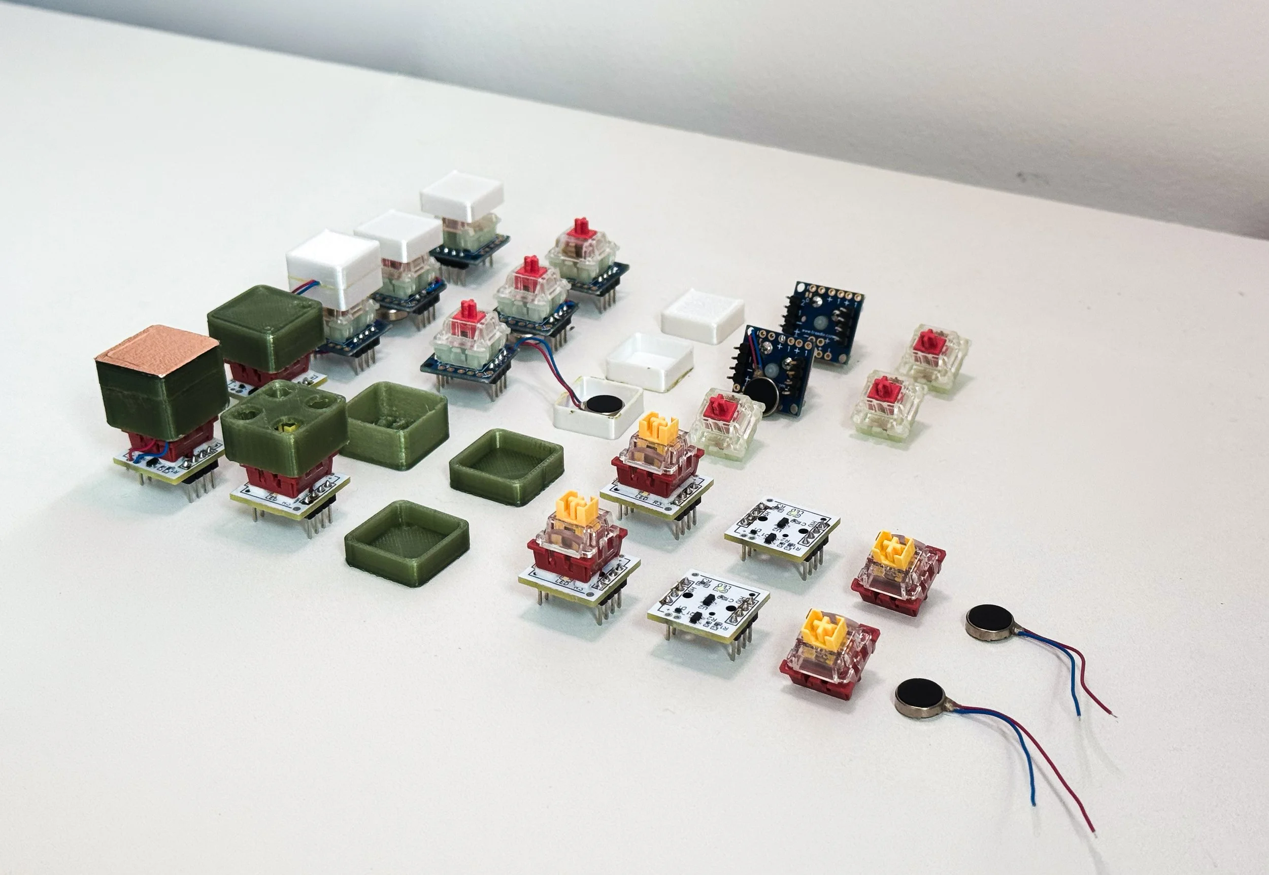 An array of electronic components and prototypes on a white surface, including switches, circuit boards, coils, and wiring.
