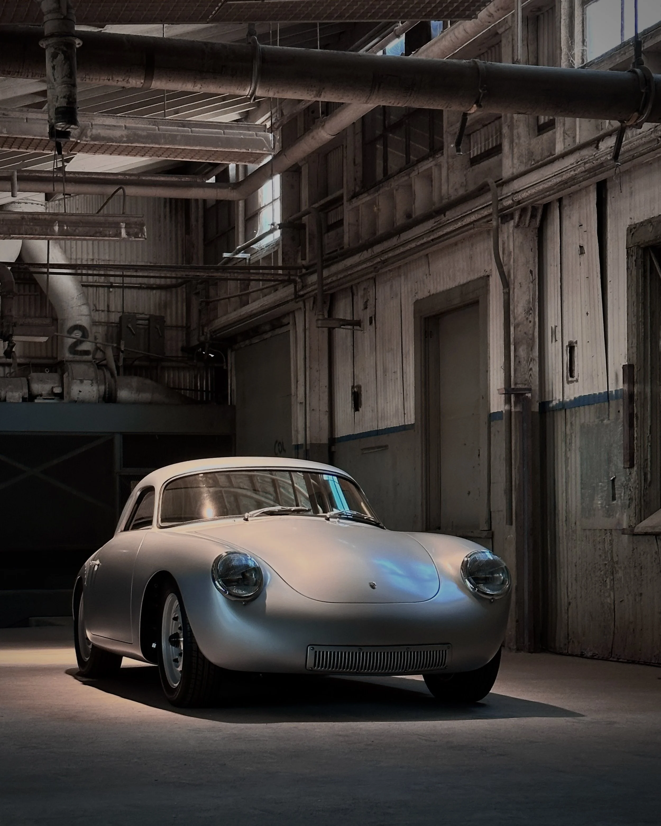 A vintage sports car parked inside an industrial garage with exposed pipes and concrete walls.