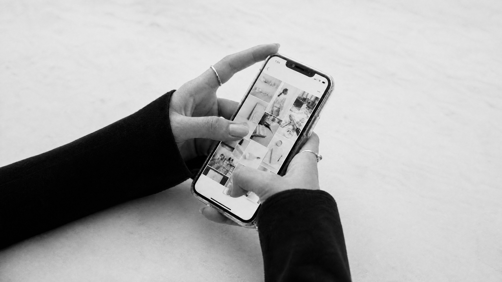 Black and white photo of a person holding a smartphone, browsing through a photo gallery or social media app.