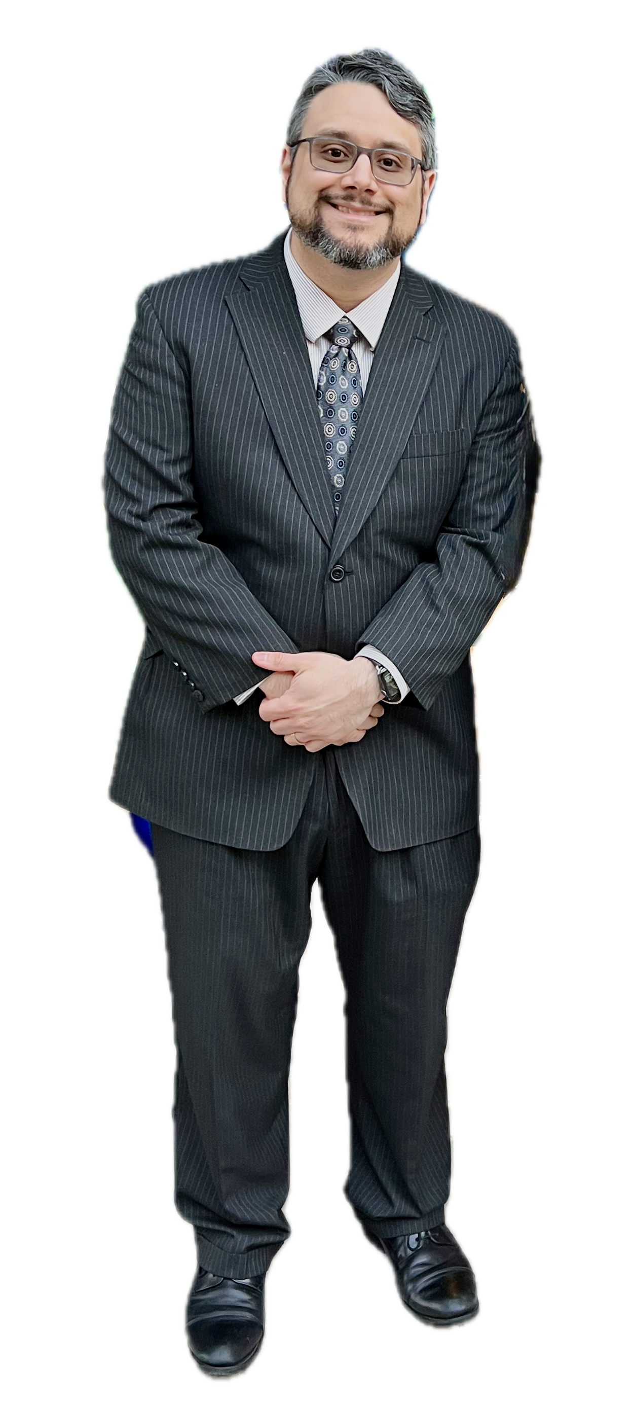 José Pitti in a pinstripe suit, white shirt, and patterned tie smiling, standing with hands clasped, wearing glasses and black dress shoes.