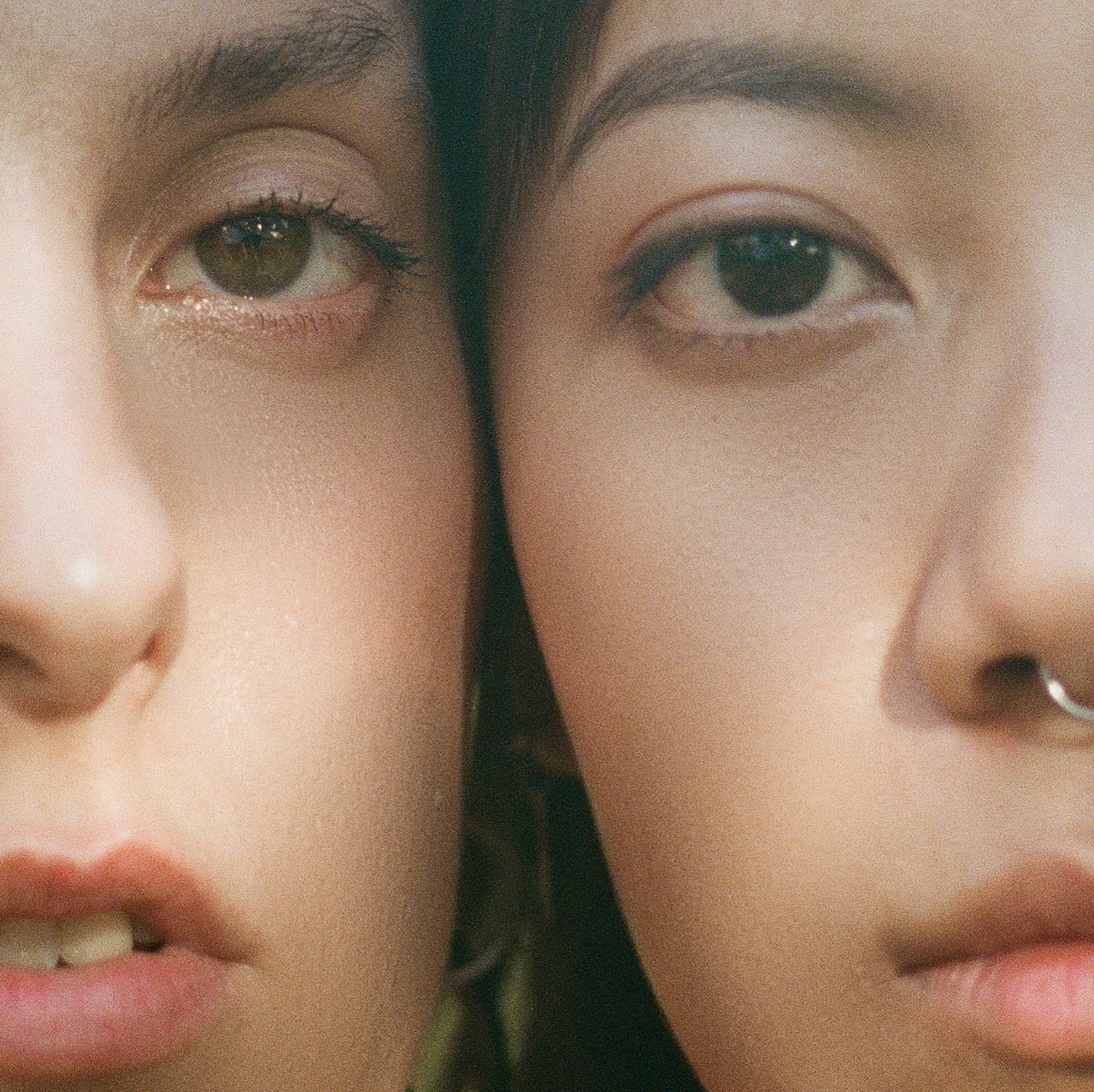Close-up of two women's faces with their eyes and noses touching, showcasing makeup and skin details.