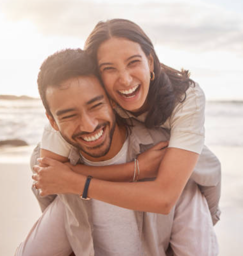 A happy couple smiling and embracing on the beach during sunset.