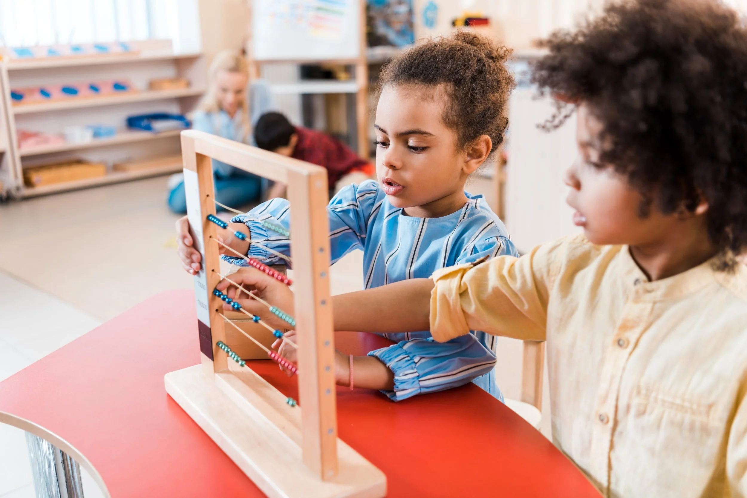 Children playing with a wooden bead maze toy at a classroom table.