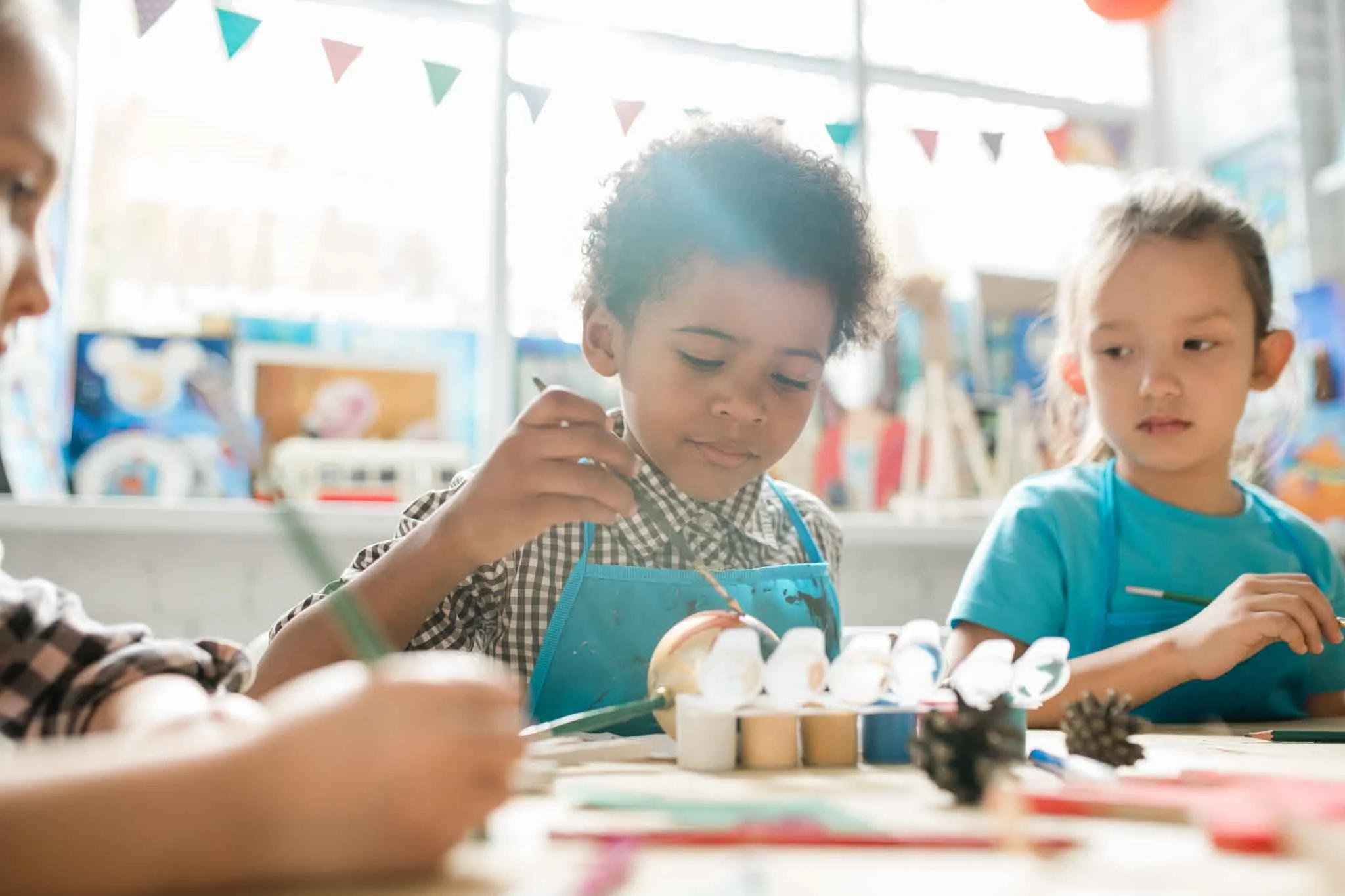 Children participating in a craft activity at a table, with colorful decorations hanging in the background.