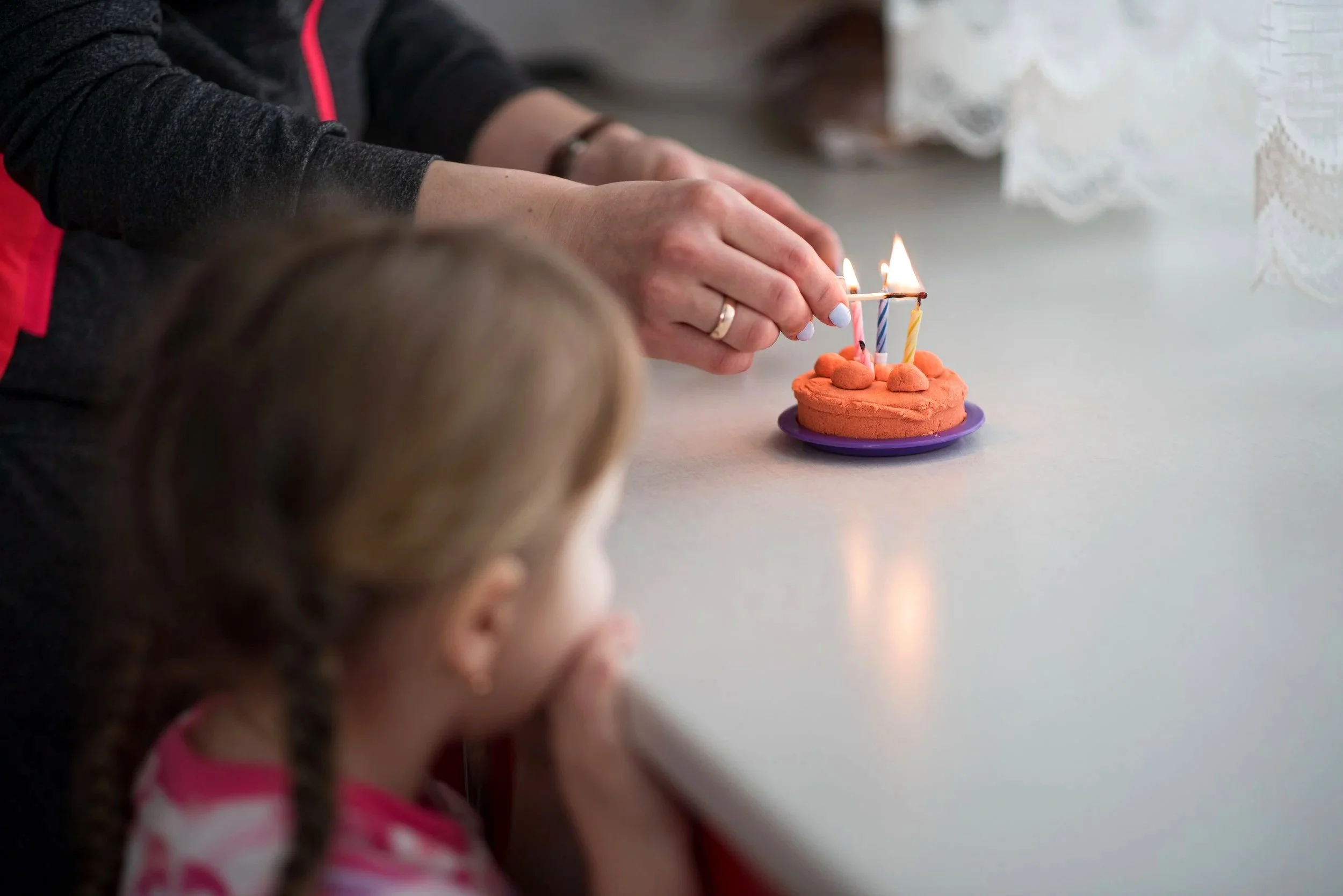Person lighting birthday candles on a small cake with a matchstick.