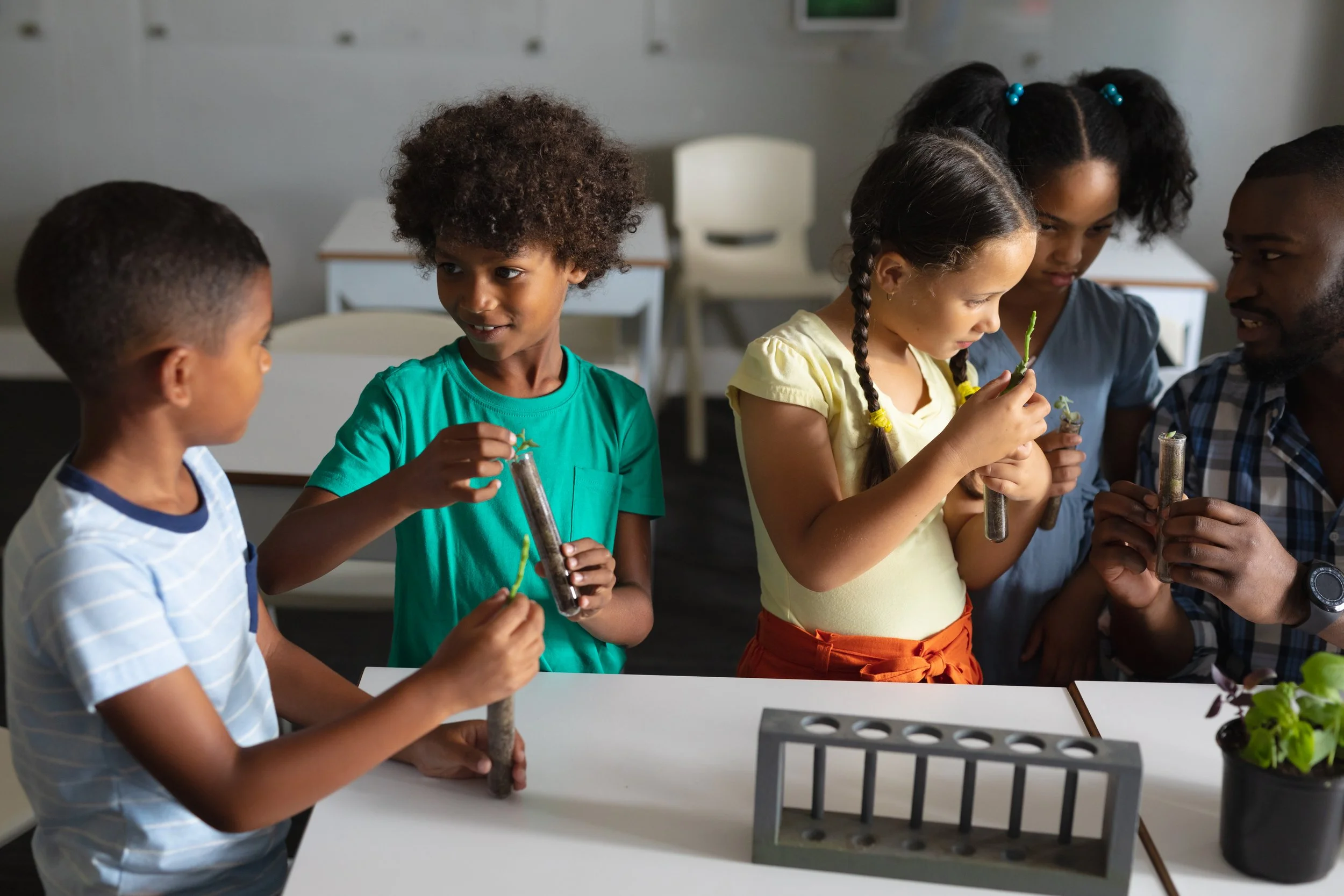 Children and a teacher conducting a science experiment with plants and test tubes in a classroom.