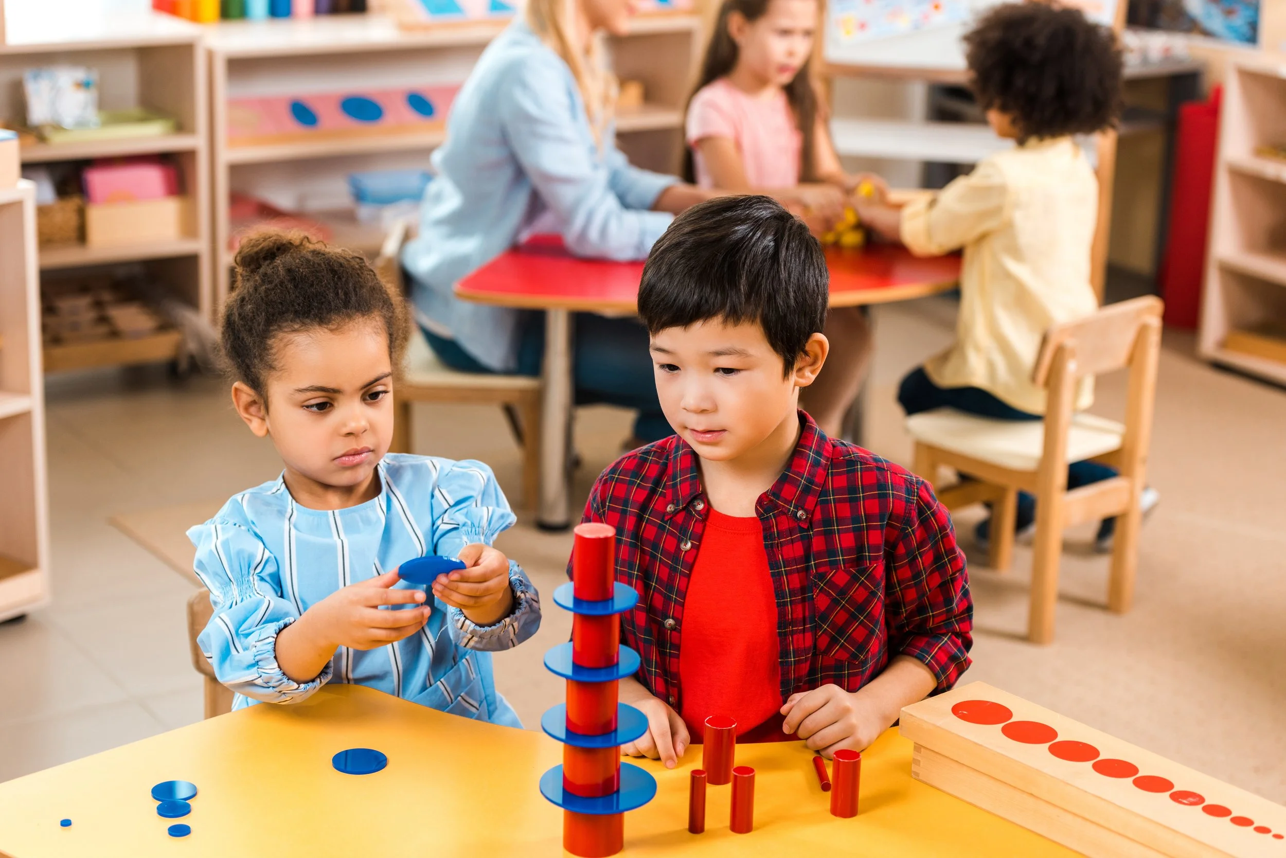 Children playing a marble game at a yellow table in a classroom.