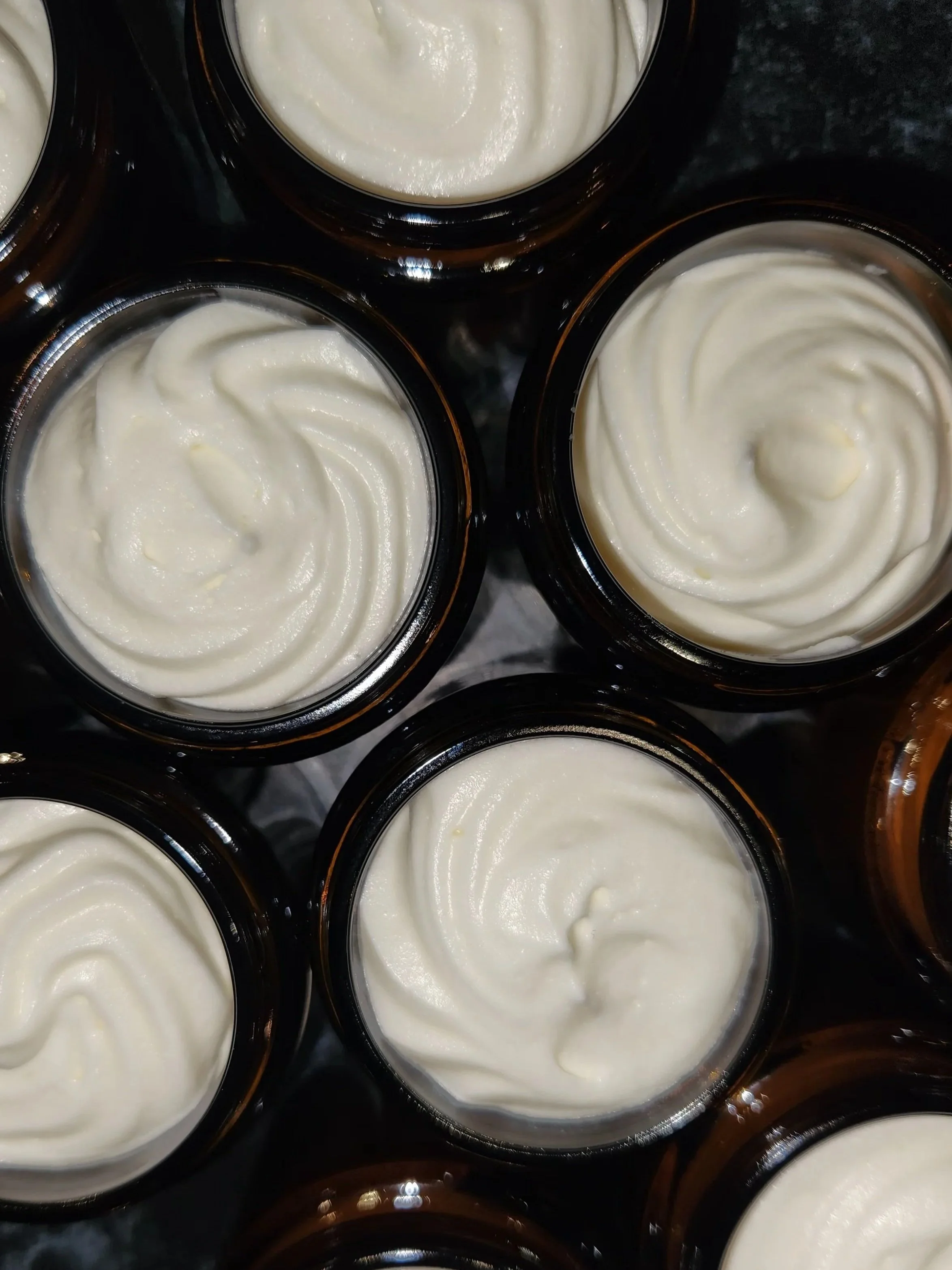 Multiple small containers filled with white cream or mousse on a black surface.