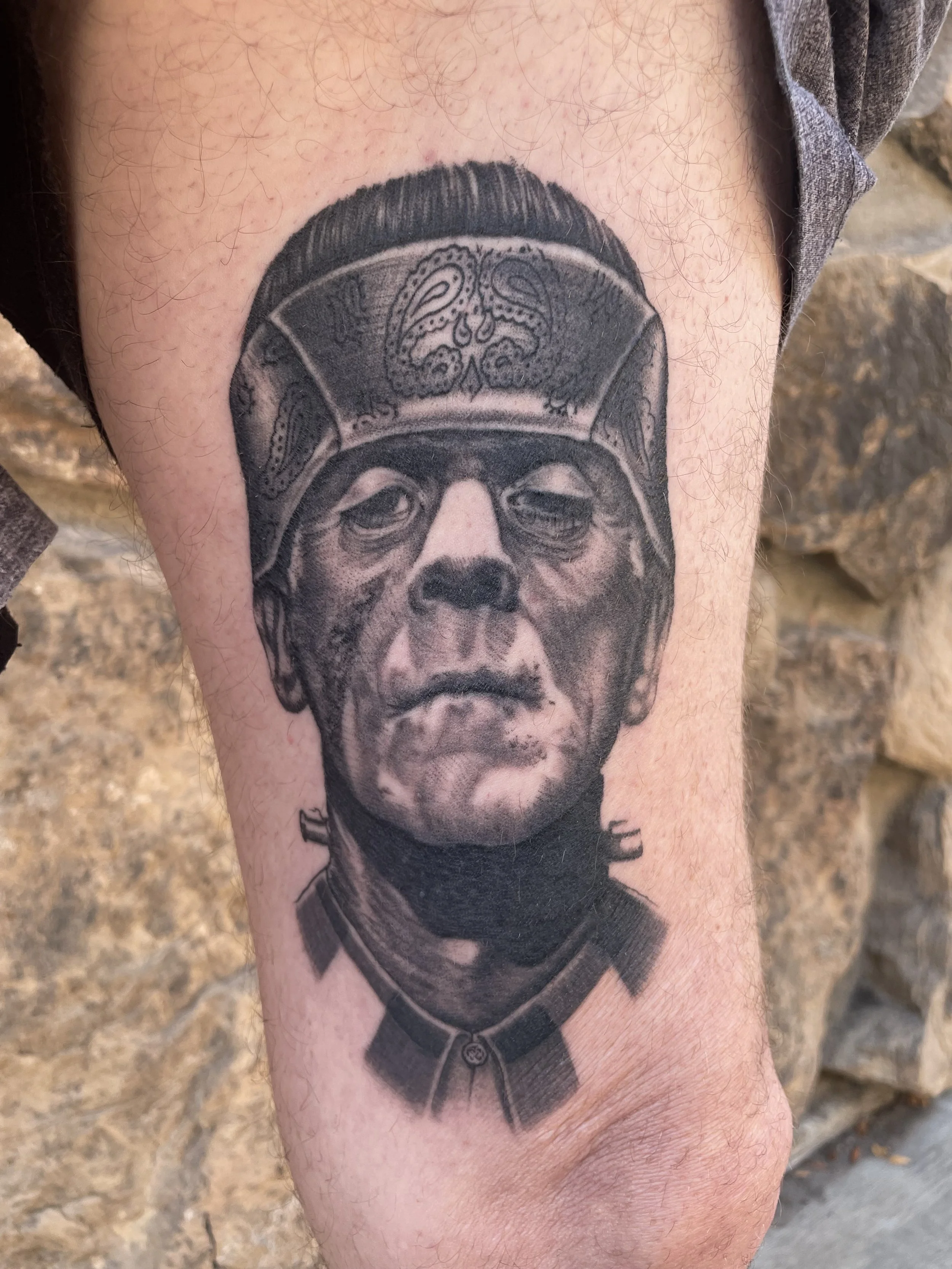 Black and gray tattoo of a man's face in military uniform on person's upper arm.