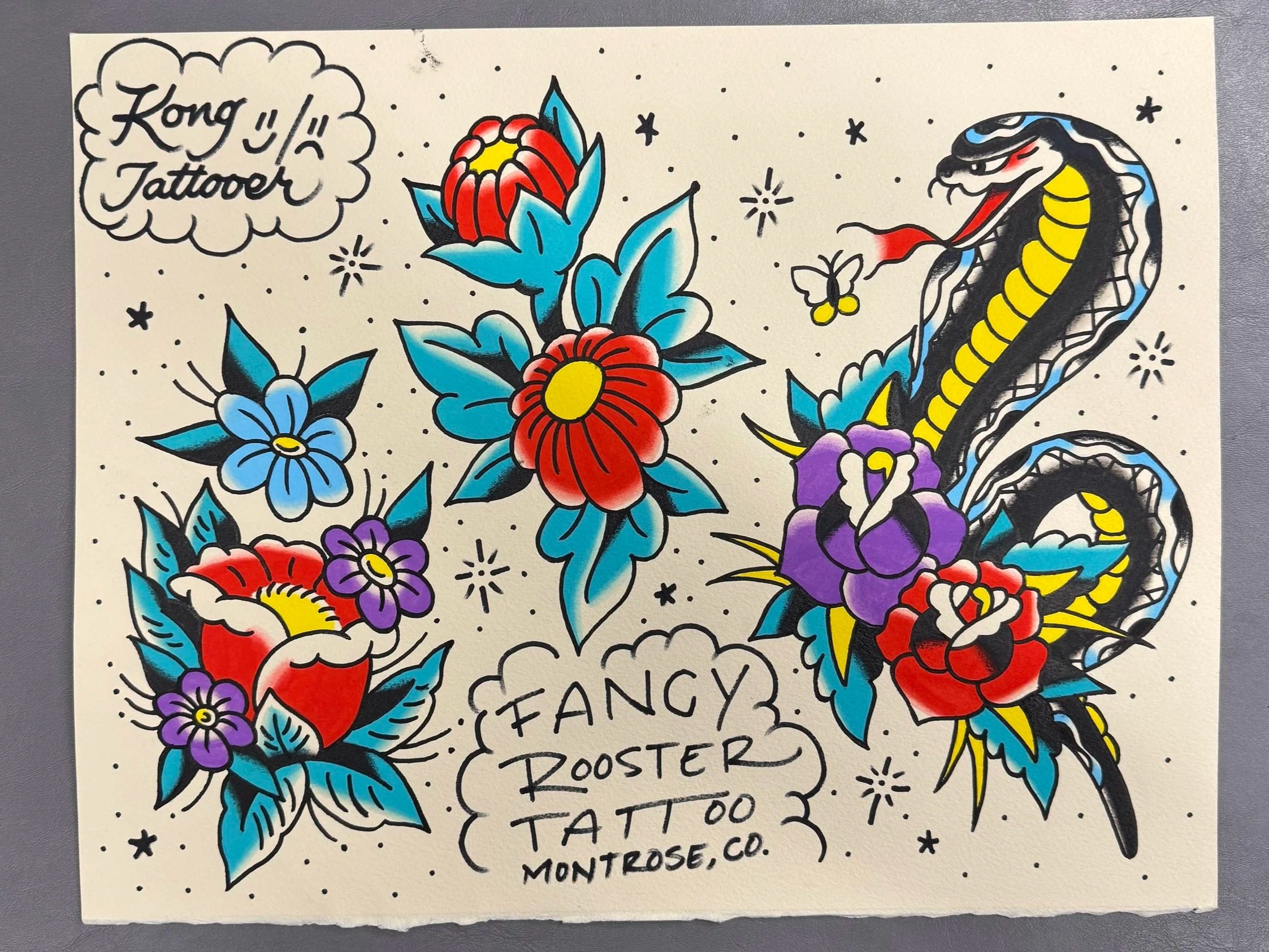 Colorful traditional tattoo artwork featuring various flowers such as roses and violets, with a snake and a butterfly, and text that reads 'Kong Tattoos' and additional descriptive words.