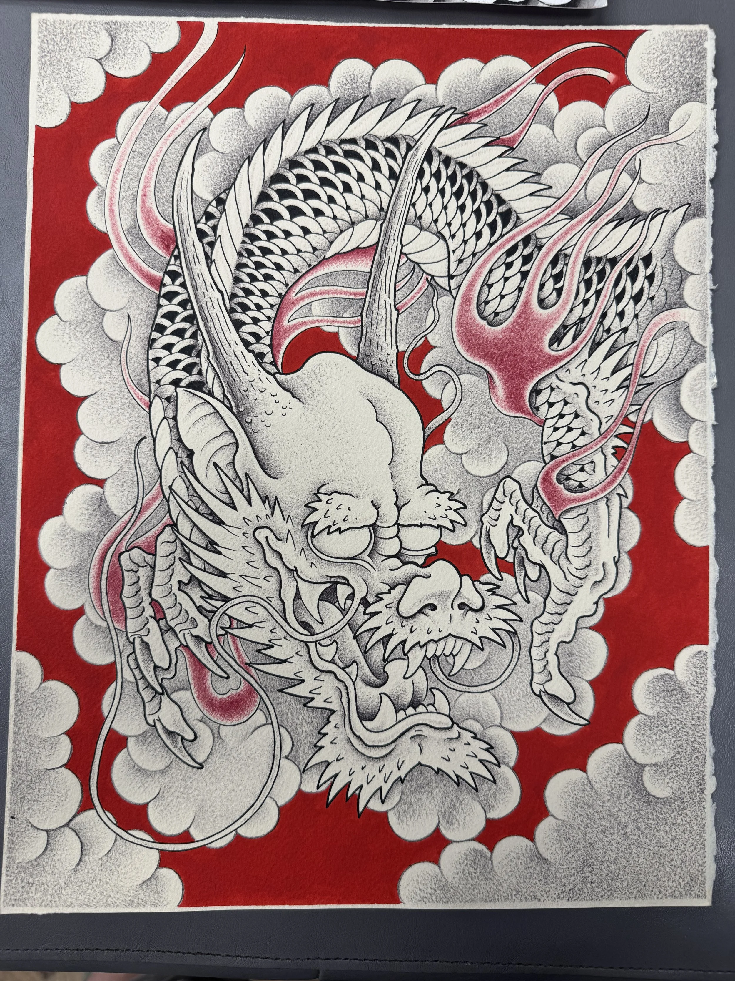 A detailed black and white drawing of a traditional Japanese dragon surrounded by clouds on a red background.