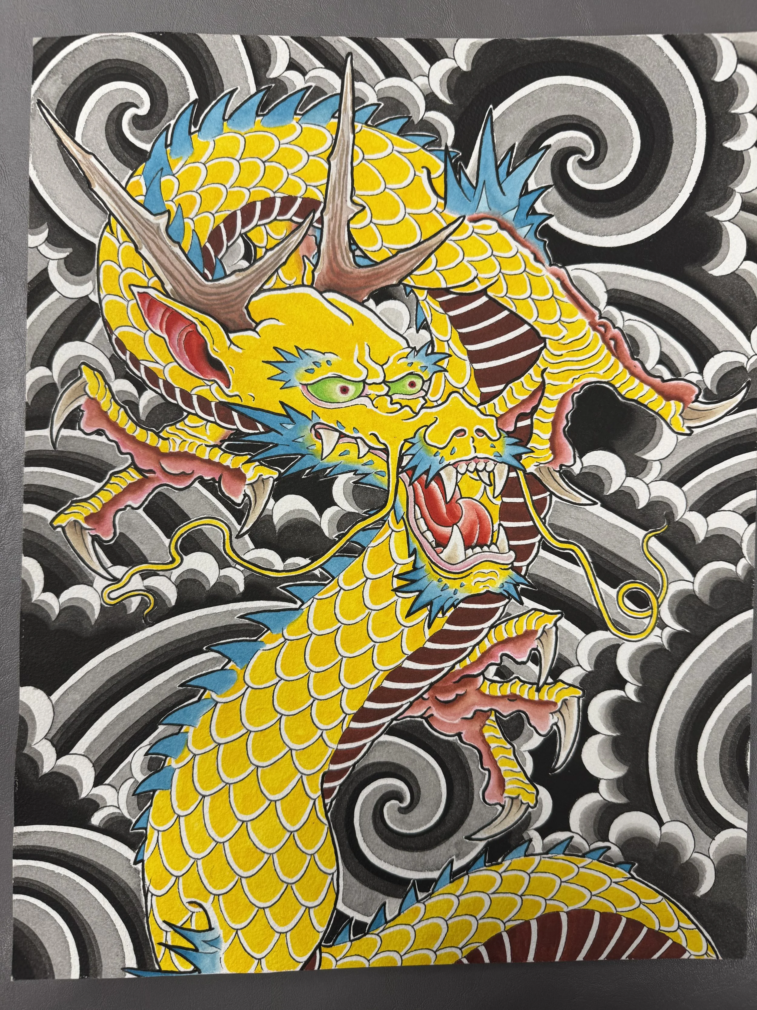 Colorful artwork of a fierce dragon with yellow scales, blue spines, and red accents, surrounded by swirling black and white cloud patterns.