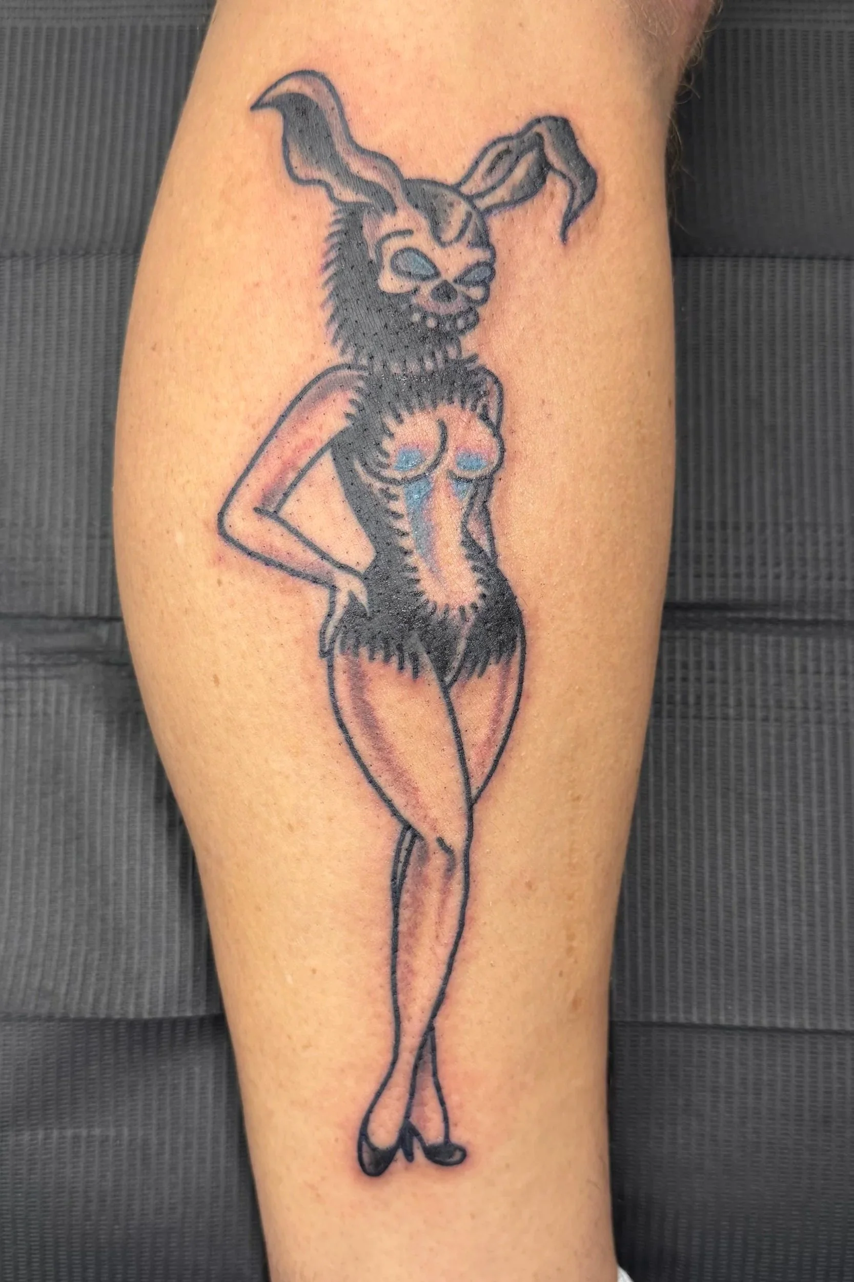 Tattoo of a cartoonish fox woman with animal features, including fox ears and tail, black outlines, and shaded areas, on a person's arm.