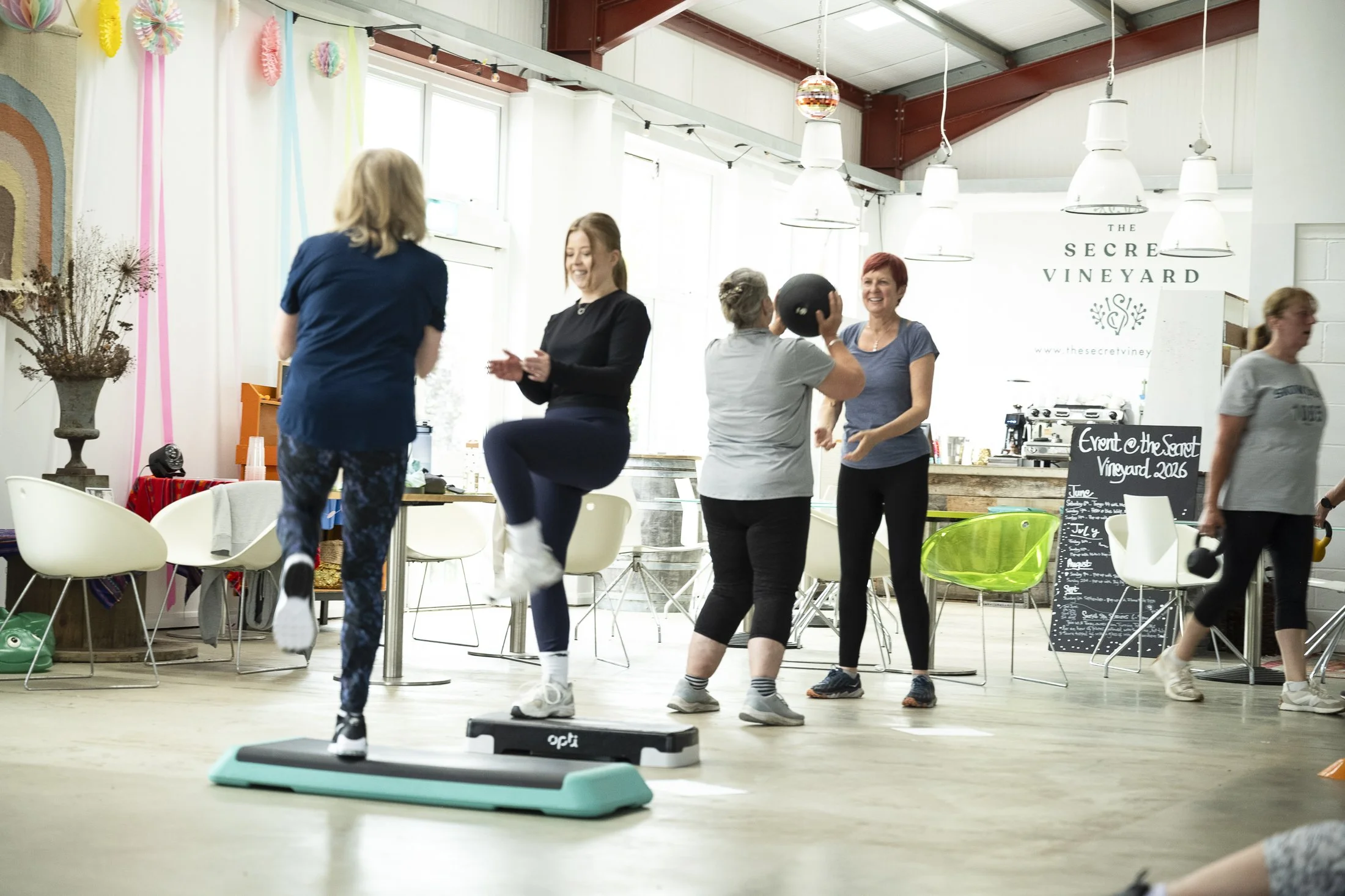 Group of women engaging in fitness activities in a bright, indoor space with natural light, white walls, and modern decor.