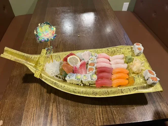 Sushi arranged on a golden boat-shaped platter with sushi rolls, sashimi, lemon slices, wasabi, and garnishes, sitting on a wooden table.