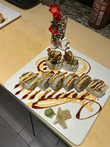 Plate of sushi rolls with drizzled sauces, wasabi, and pickled ginger on a white square plate.