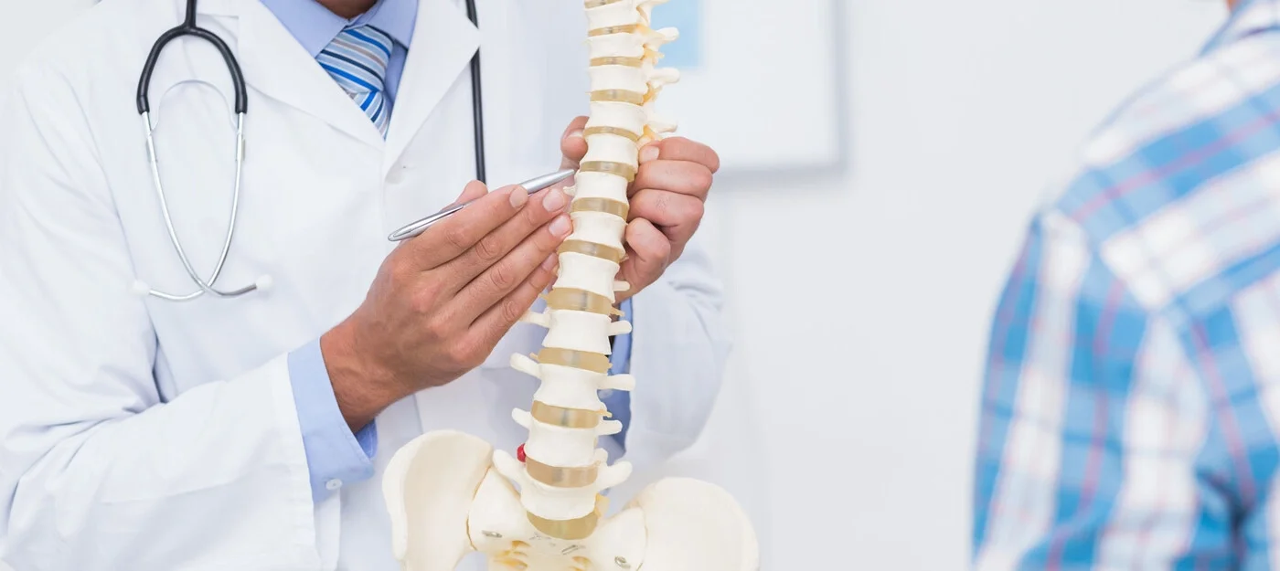 Doctor explaining the human spine model to a patient in a medical office.