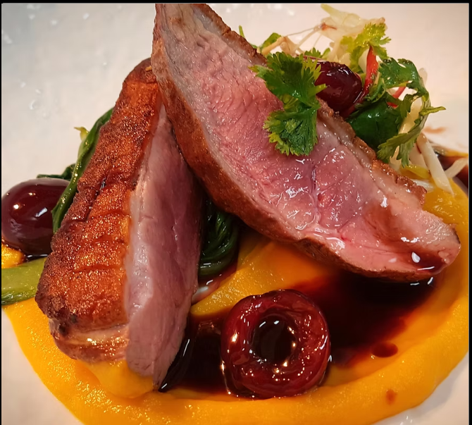Two slices of seared tuna steak on a bed of whipped sweet potato, garnished with cherry tomatoes, greens, and cilantro, topped with a drizzle of balsamic glaze.