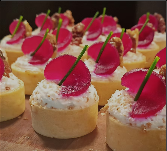 Mini cheesecakes topped with pink gelatin, a green garnish, and crumbly bits on a wooden surface.