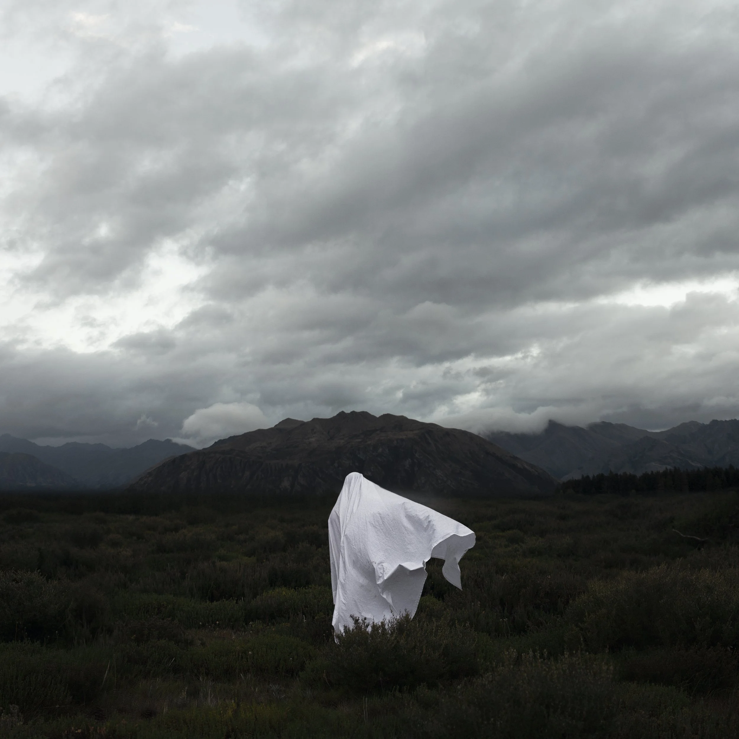 A mountain landscape under a cloudy sky with some fog, and a white tent in the foreground.