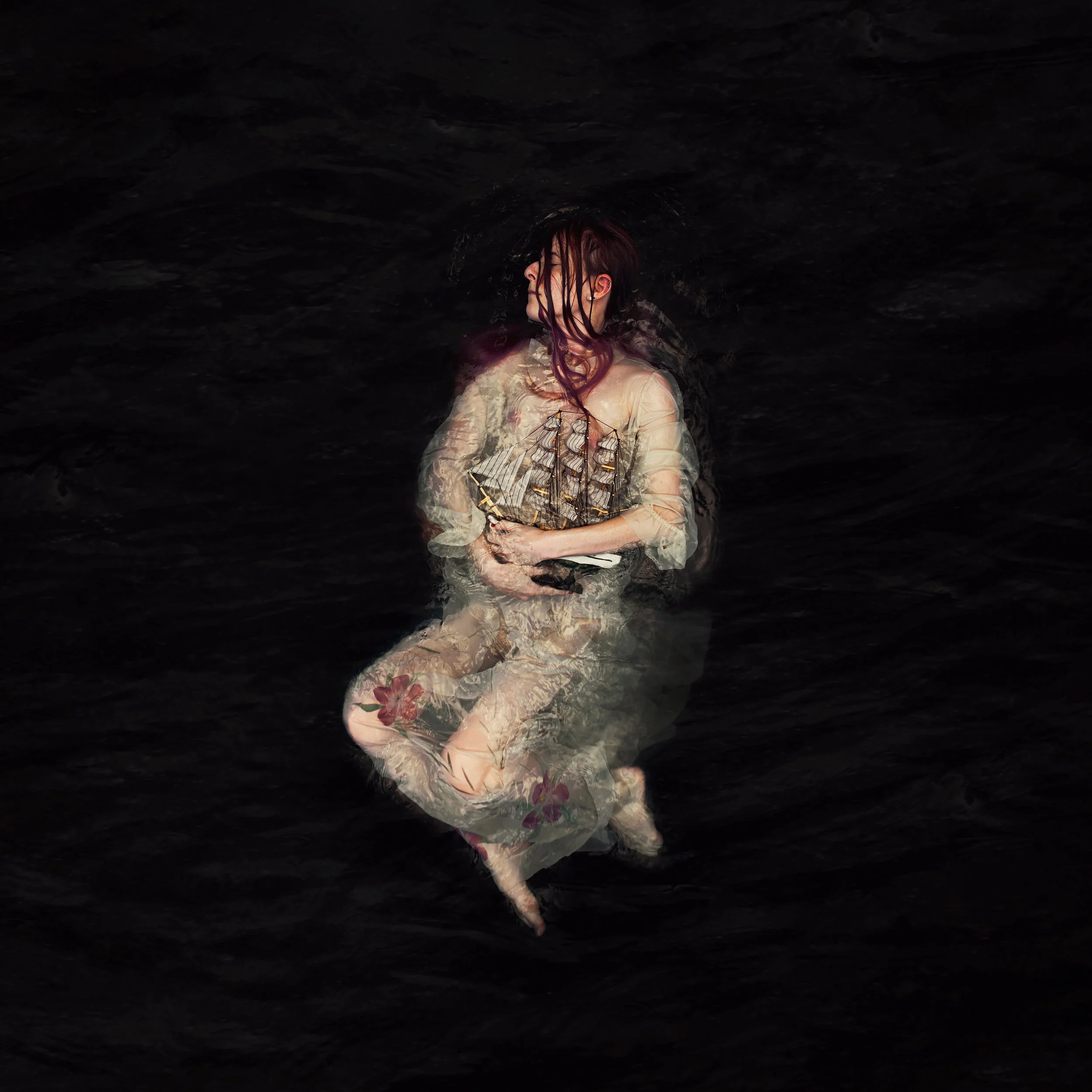 A woman with wet hair in water, wearing a white dress with floral patterns, tilting her head back with closed eyes in darkness.