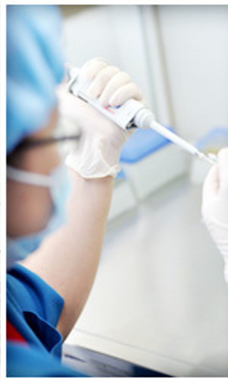 A healthcare worker wearing gloves and a face mask prepares an injection in a clinical setting.