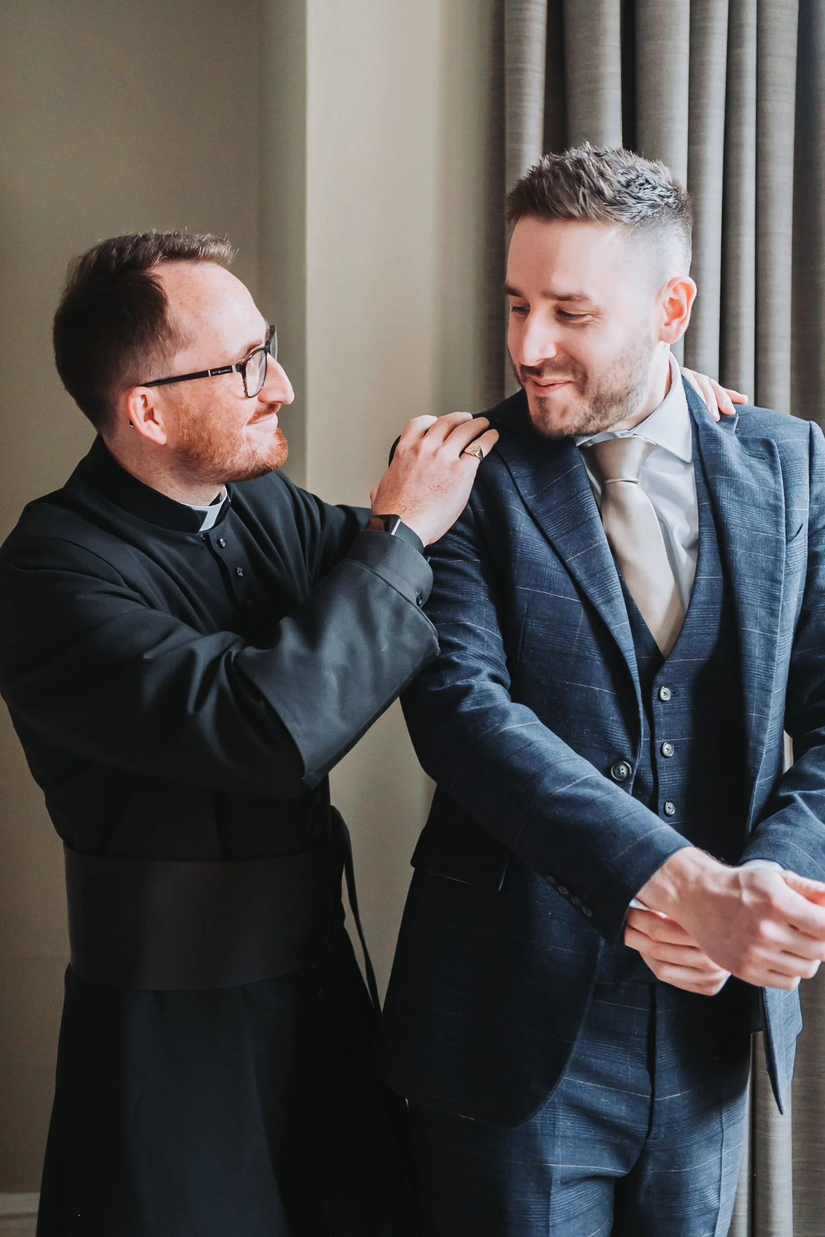 A priest places a supportive hand on the groom’s shoulder in a quiet moment before the wedding ceremony.