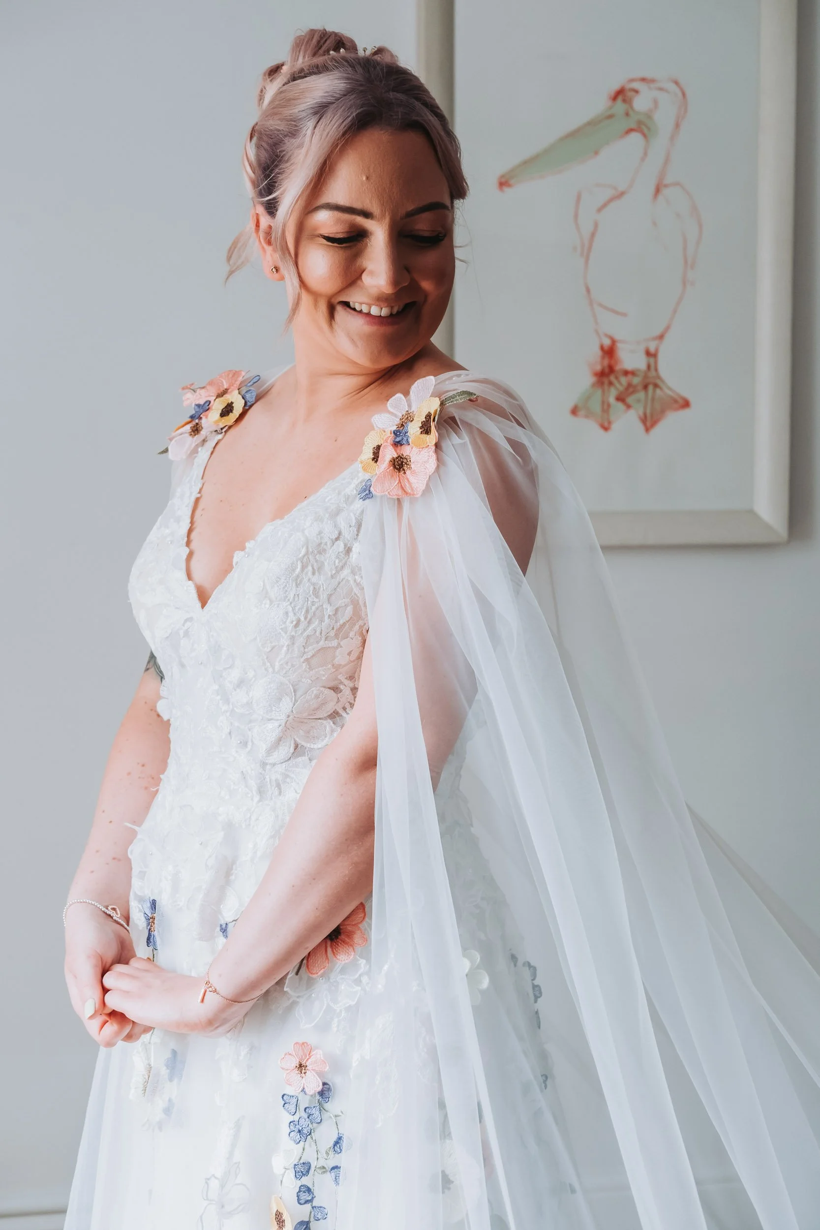 Bride smiling softly in a close-up portrait showcasing her embroidered floral wedding dress and delicate tulle cape sleeves during bridal prep.