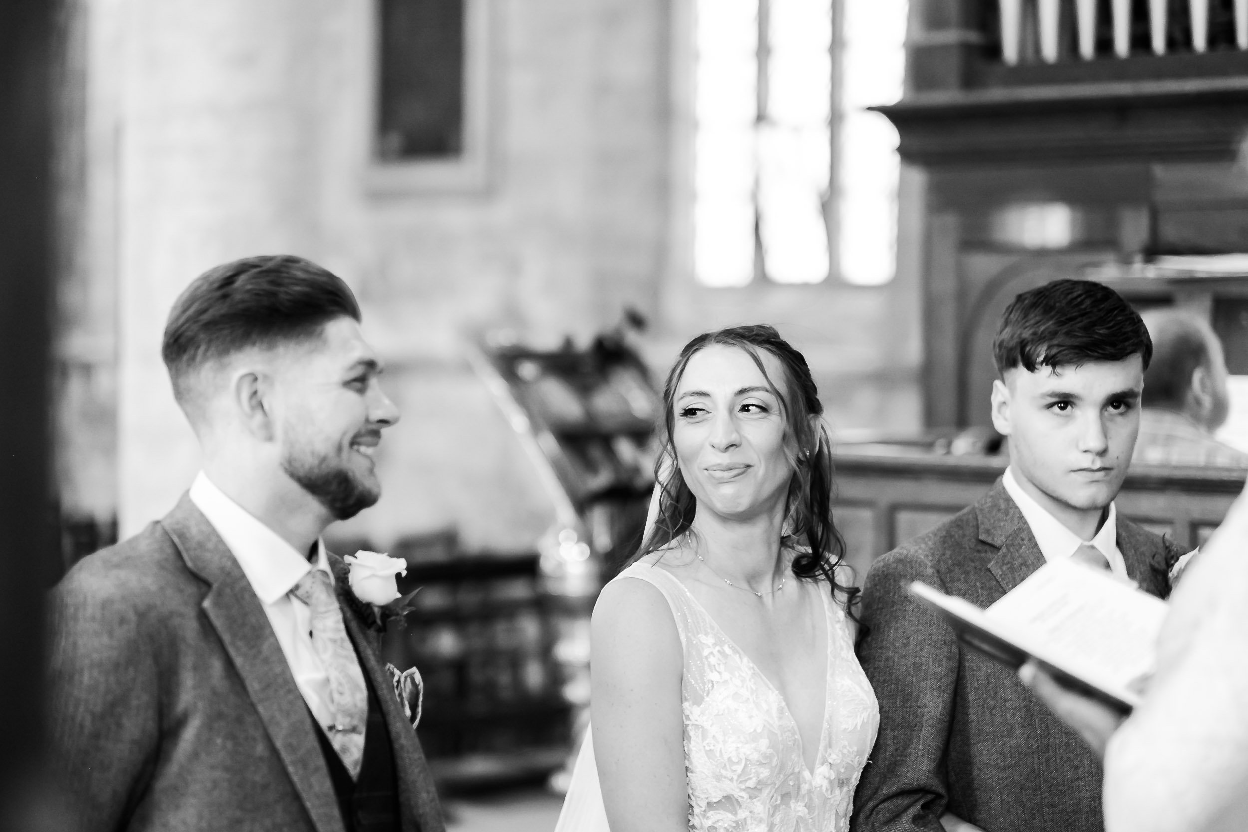 A bride and groom share a meaningful glance during their wedding ceremony in a church, surrounded by their bridal party.