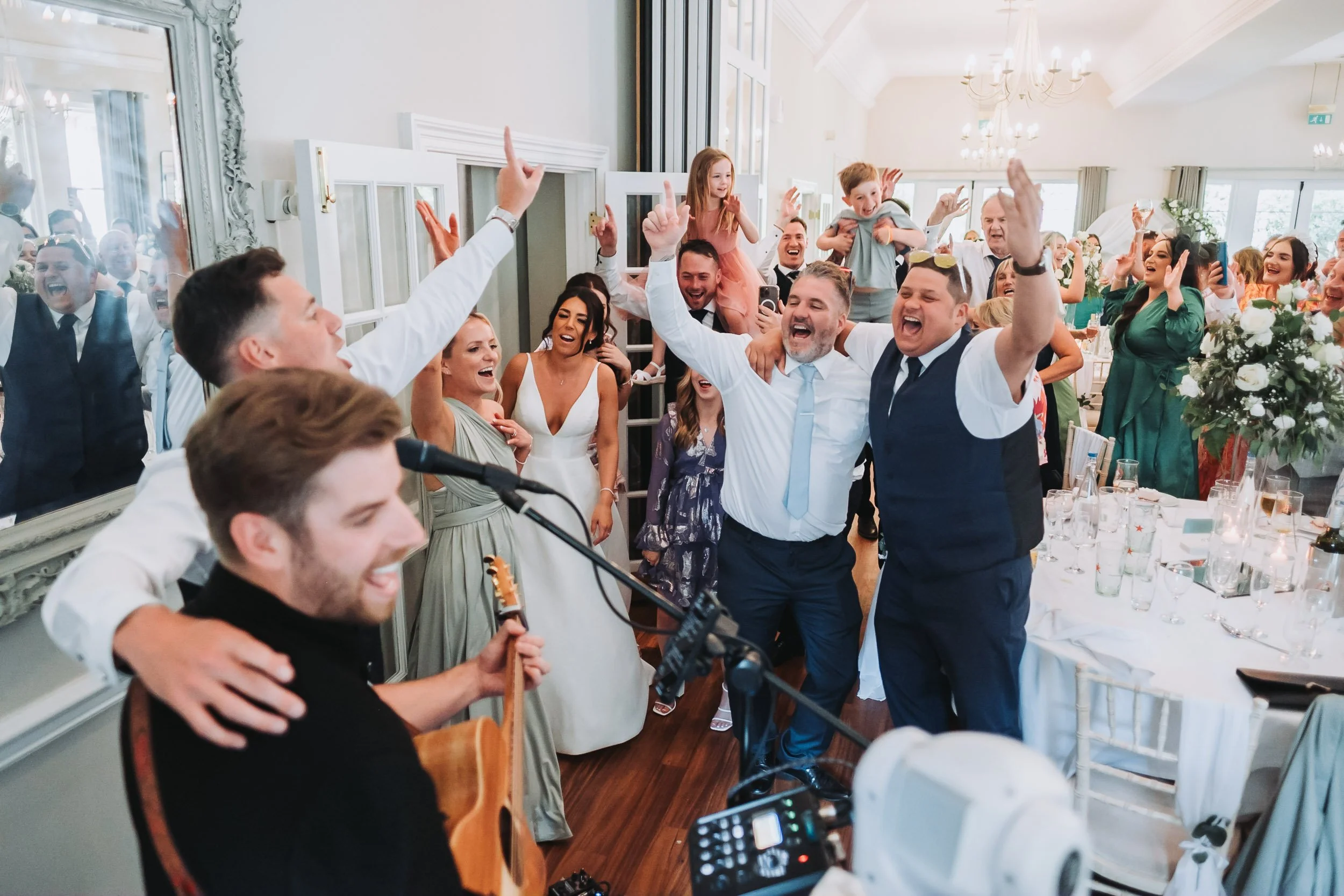 Wedding guests singing and dancing along with a live band during a high-energy wedding reception.