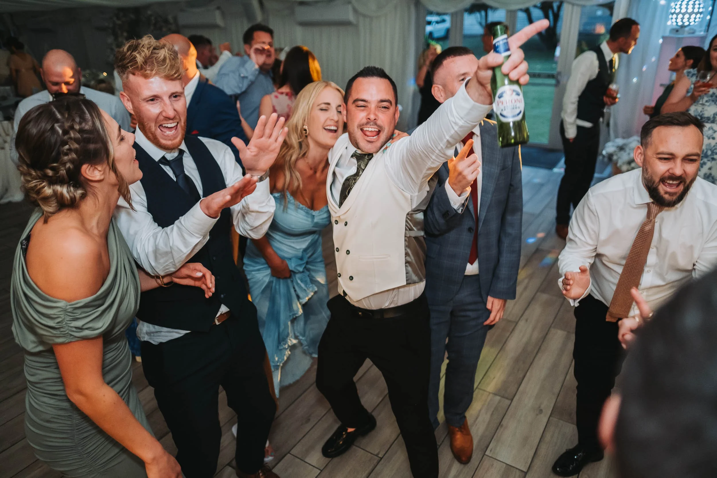 Group of people dancing and celebrating at a party or social event indoors, with some holding drinks and smiling.