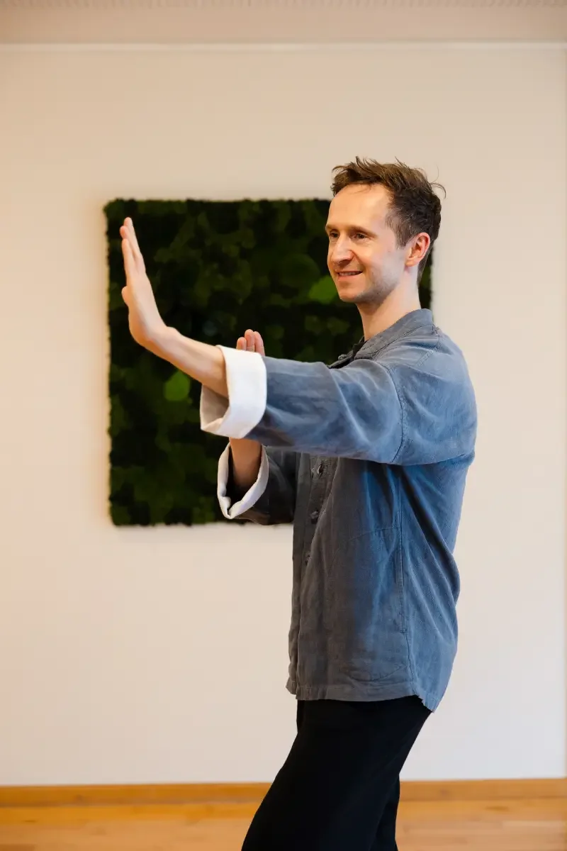 A man practicing Tai Chi indoors with a green decorative wall behind him.