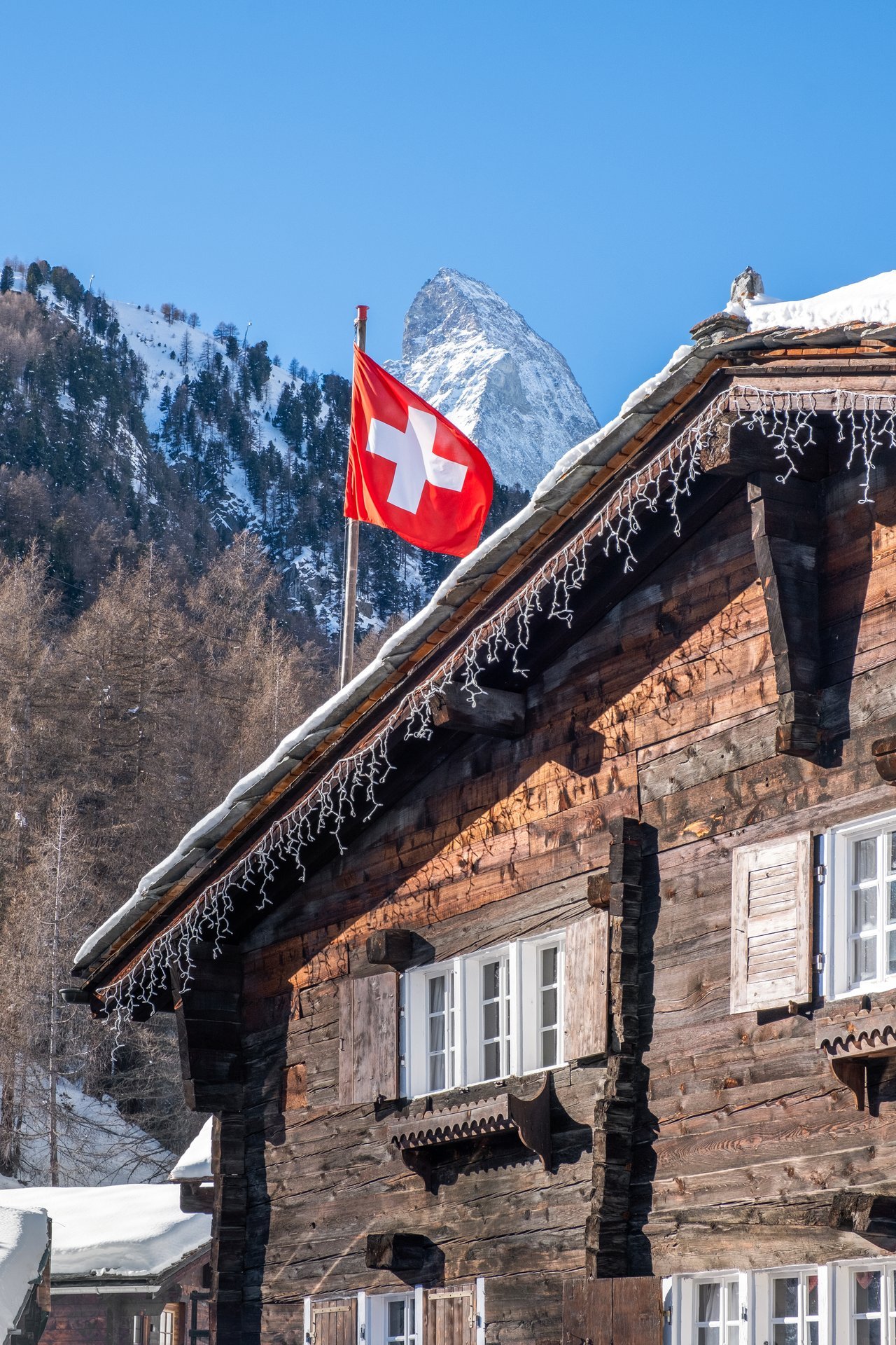 Schneebedecktes Chalet in den Schweizer Alpen mit Schweizer Flagge, im Hintergrund Berge und blauer Himmel.