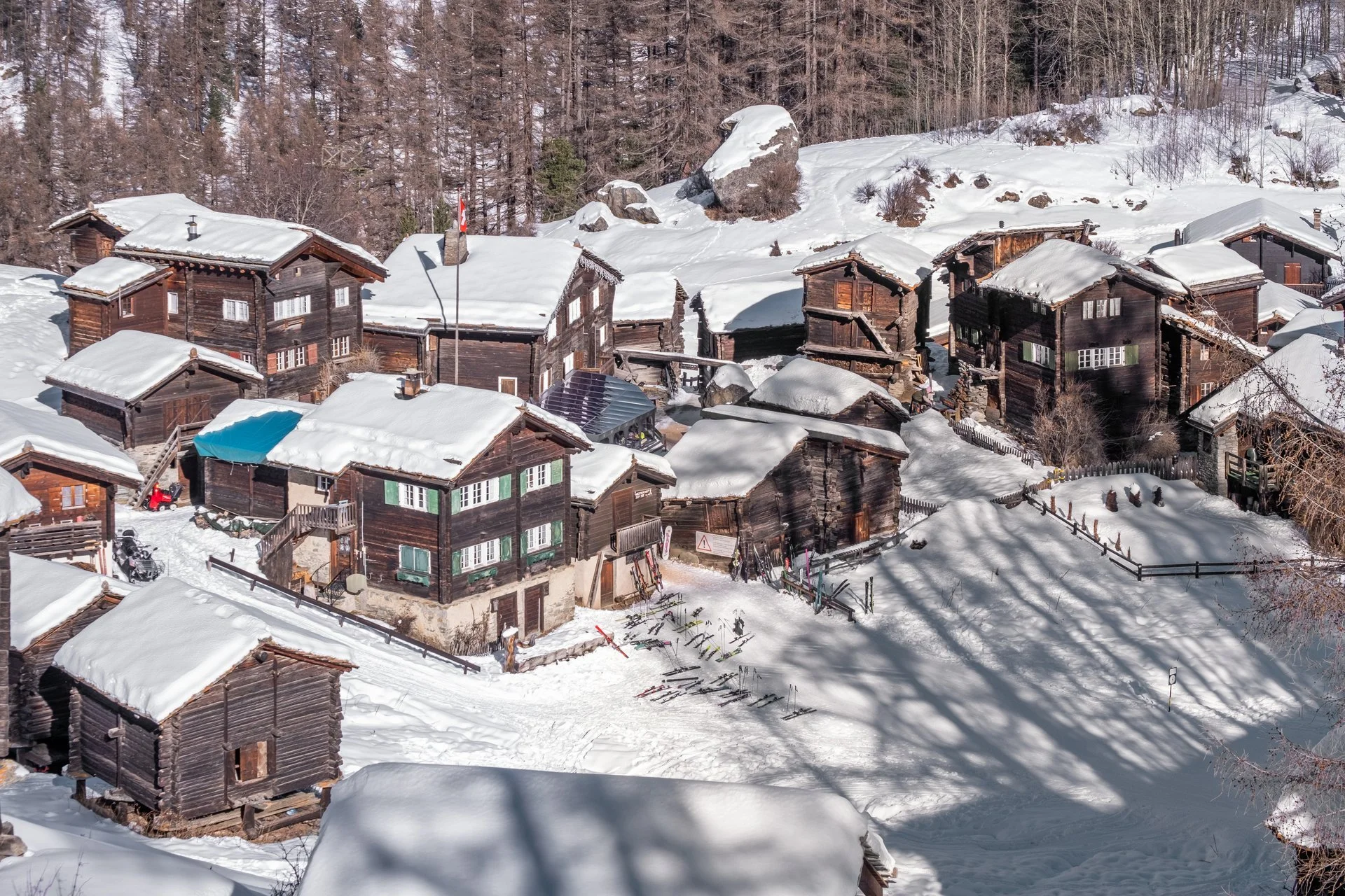 Schneebedeckte Chalets in einem verschneiten Bergdorf, umgeben von Tannenbäumen und Felsen im Winter.