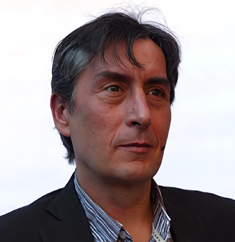 Retrato de un hombre con cabello gris y oscuro, usando saco y camisa a rayas, con fondo blanco.