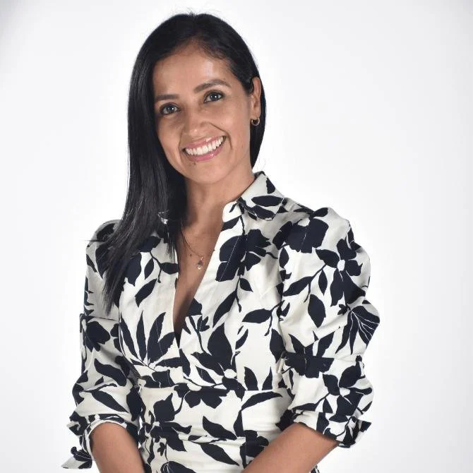 Mujer con cabello negro, sonrisa, vestida con blusa blanca con estampado de hojas negras, fondo blanco