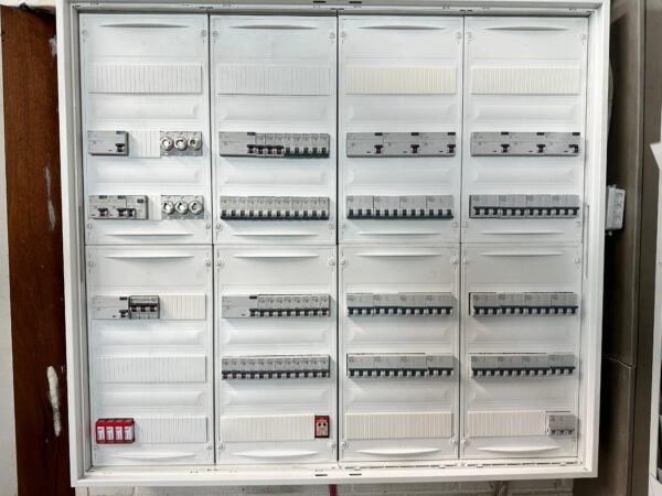 Ein elektrischer Verteilerkasten mit Sicherungen und Leitungsklemmen, mehrere Reihen von Sicherungskästen auf einem weißen Gehäuse.
