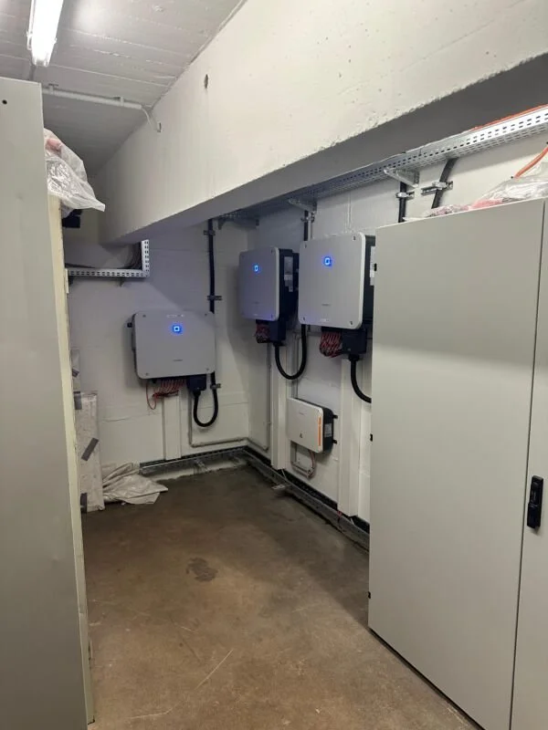 Ein Raum mit drei Wallbox-Ladestationen für Elektroautos, die an der Wand montiert sind, sowie einem weißen Schrank und Regalen an der Decke.