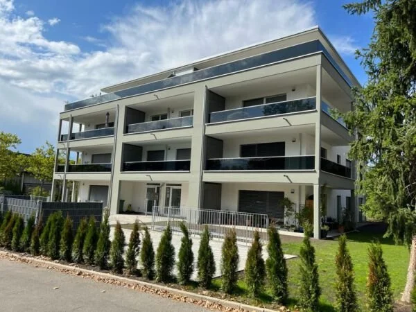 Moderne dreistöckige Wohnung mit Balkonen, umgeben von grüner Landschaft und Bäumen.